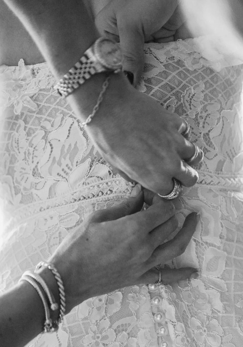 Hands fastening buttons on a lace wedding dress.