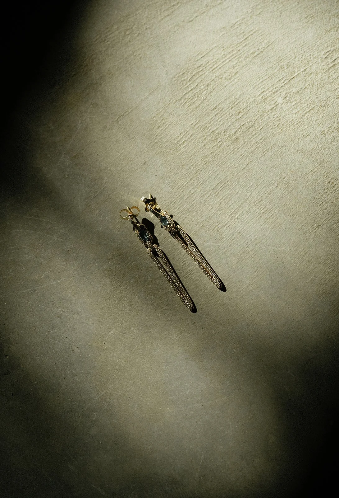 A pair of gold dangling earrings with intricate chain design on a textured surface.