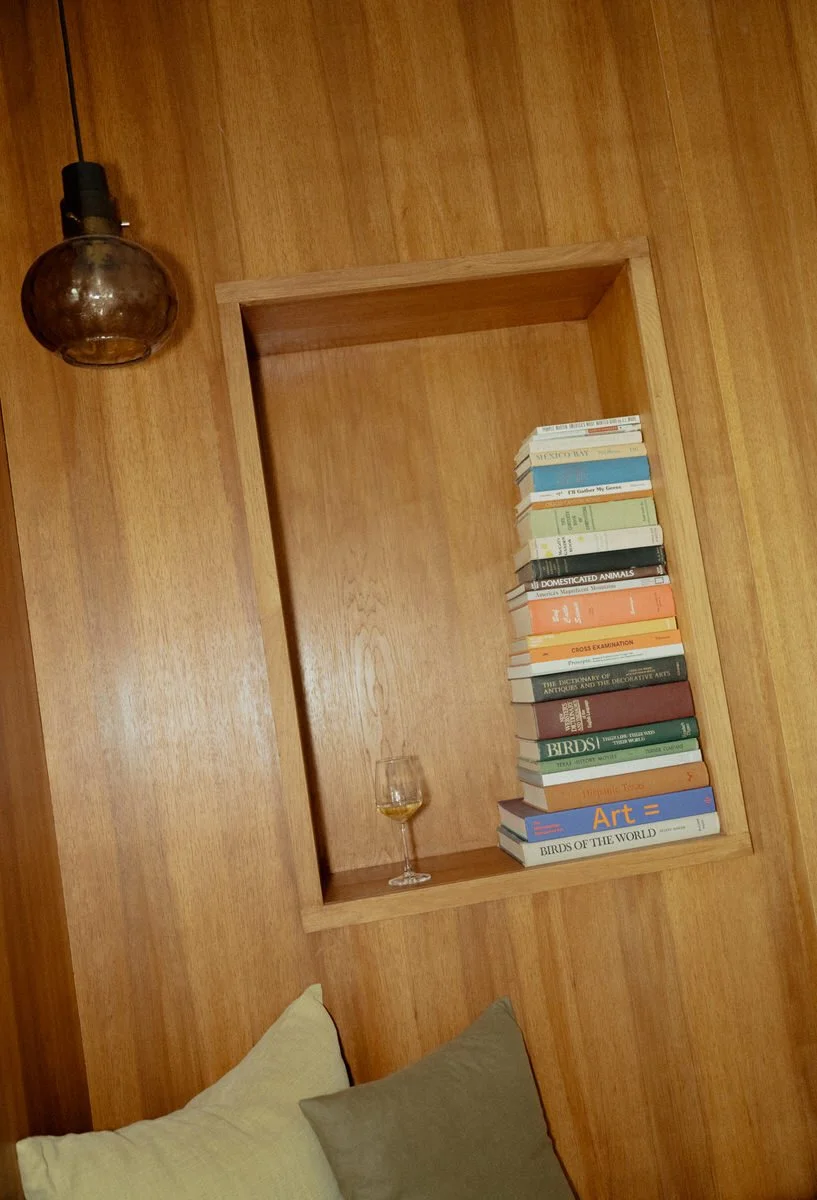 Wooden wall niche with a stack of books and an empty wine glass, pendant light, two pillows.