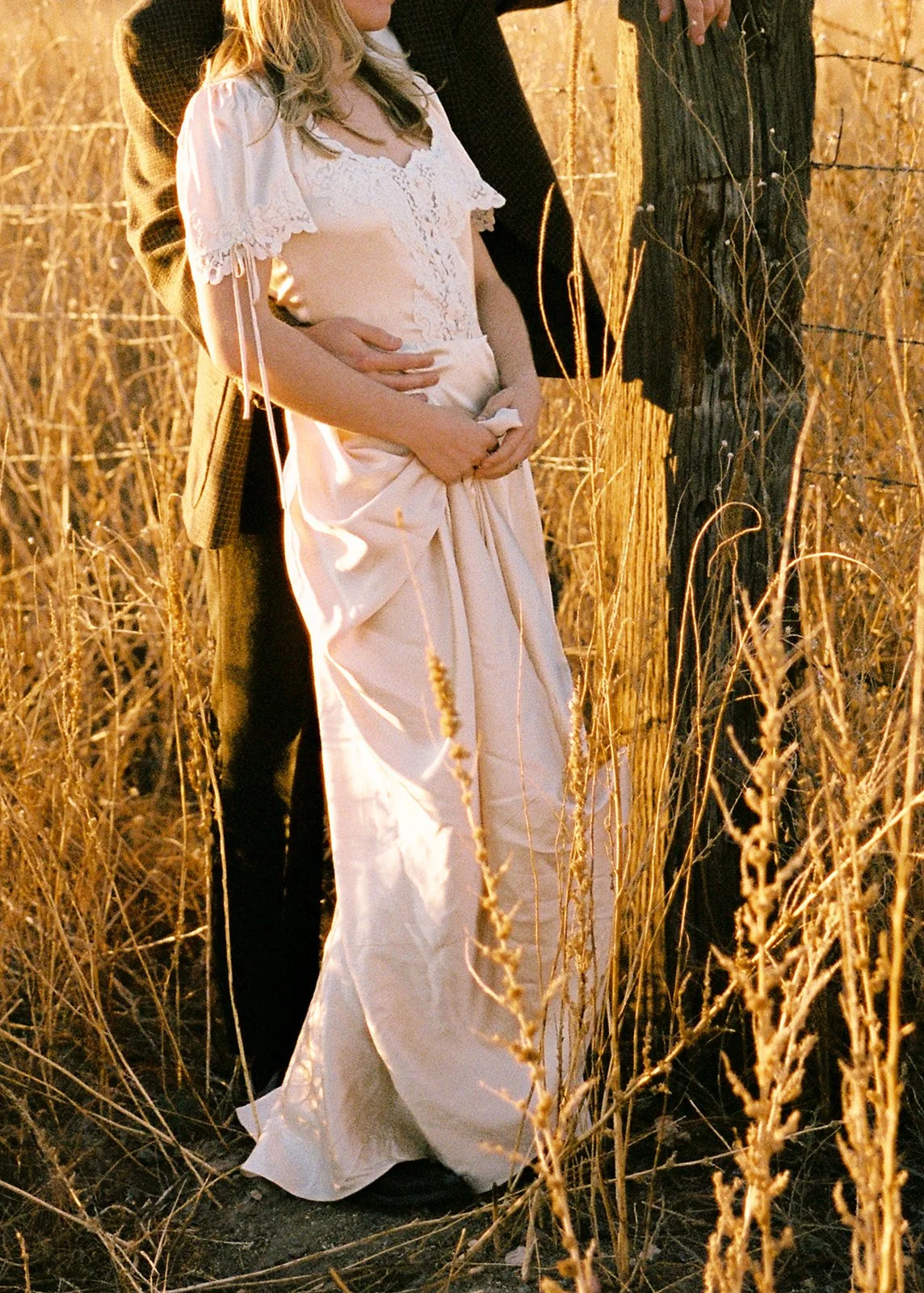 A man in a suit and woman in a silk dress standing together amongst tall yellow grass.
