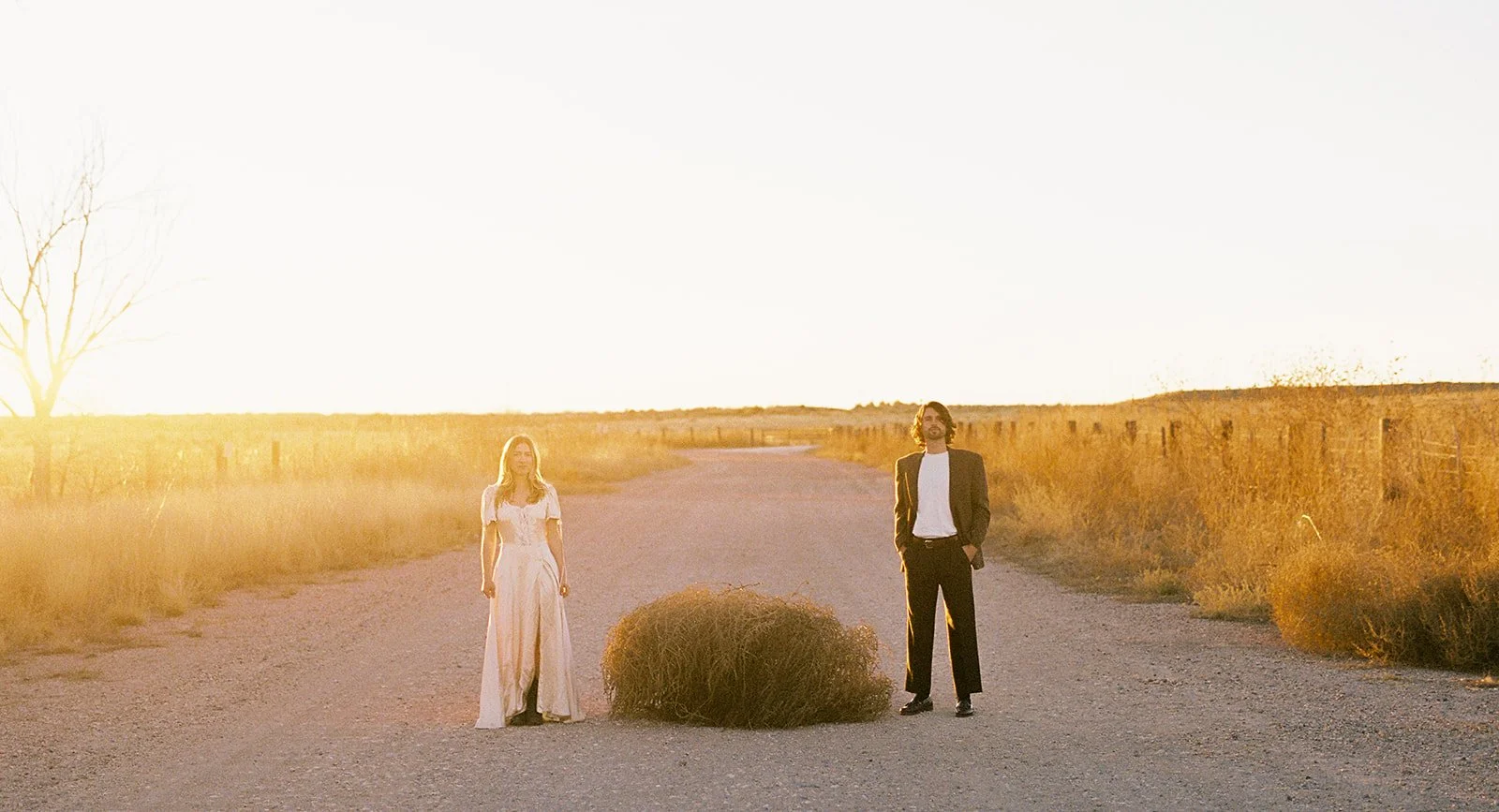 A film photo of a couple standing side by side with a giant tumbleweed in between them.