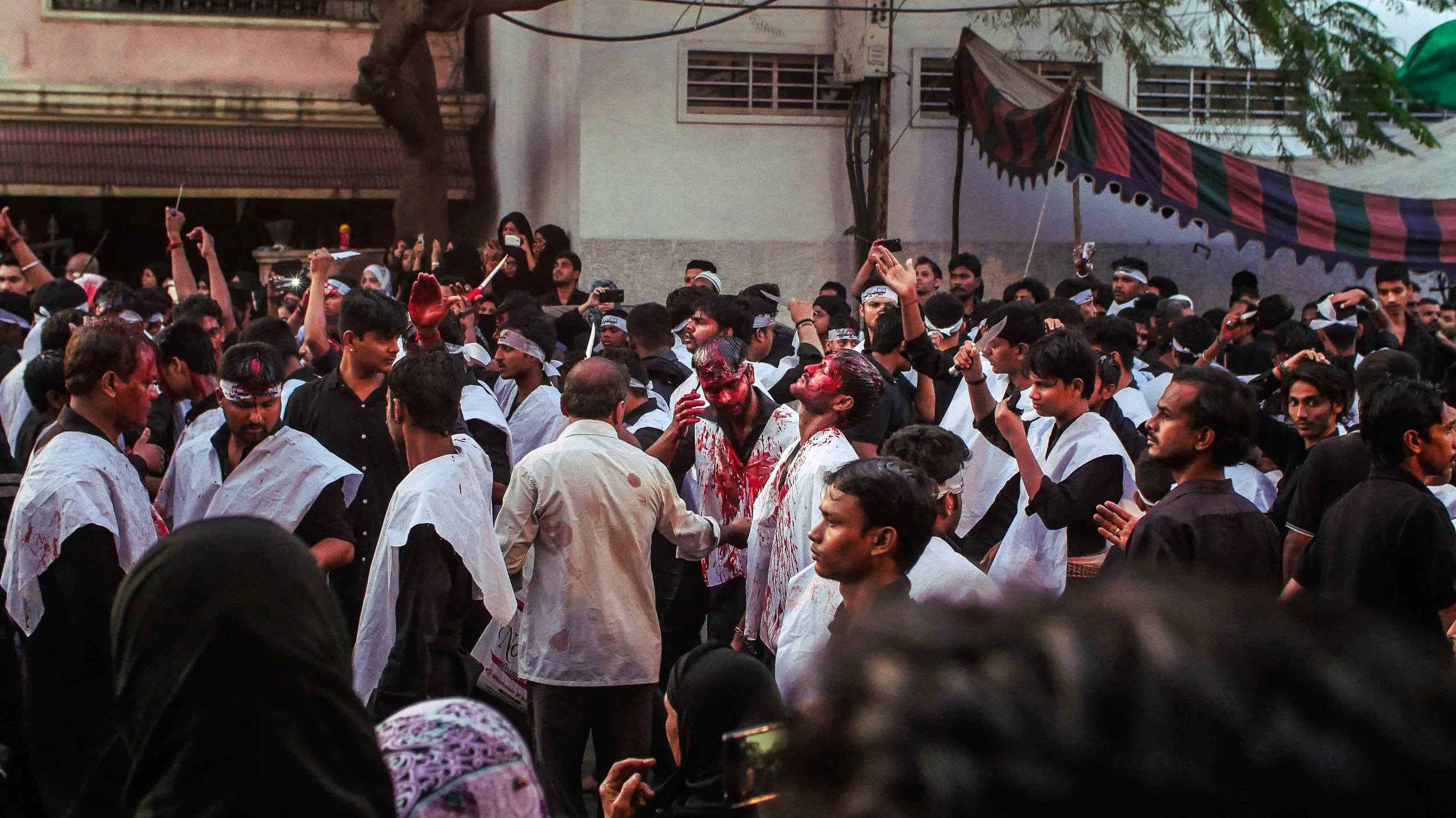 Muharram | Old City | Hyderabad. On the tenth day of Muharram, Shia muslims mark the day when Hussain abn Ali, the prophets grandson, was martyred at the Battle of Karbala in 680. Men place blades between their fingers and beat their heads and chests to a ritual drumbeat, which boys imitate but with no blades, whilst women and girls look on. In Hyderabad, the parade is peaceful but bloody. For more images and clips of this repentance ritual please contact me . 