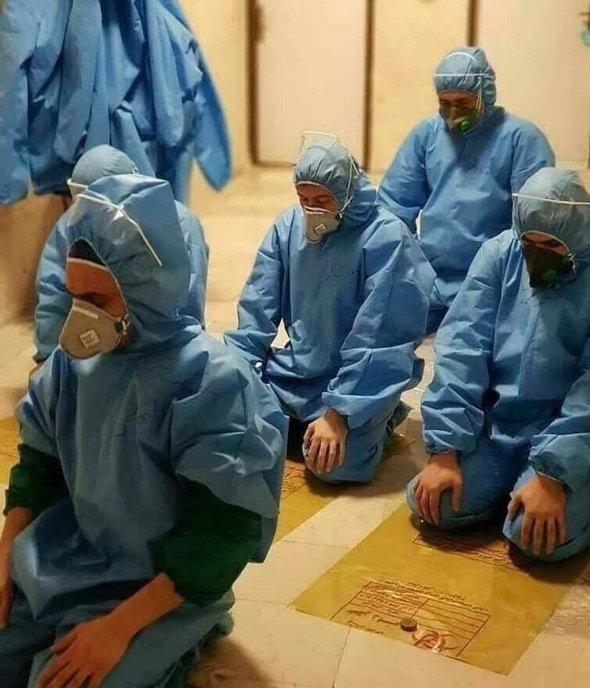 Doctors pray together in COVID-19 protective gear at the Al-Shifa Hospital in Mosul.    Photo credit: Dr. Arif Al-Azzawe &amp; Dr. Nadhim Ismael