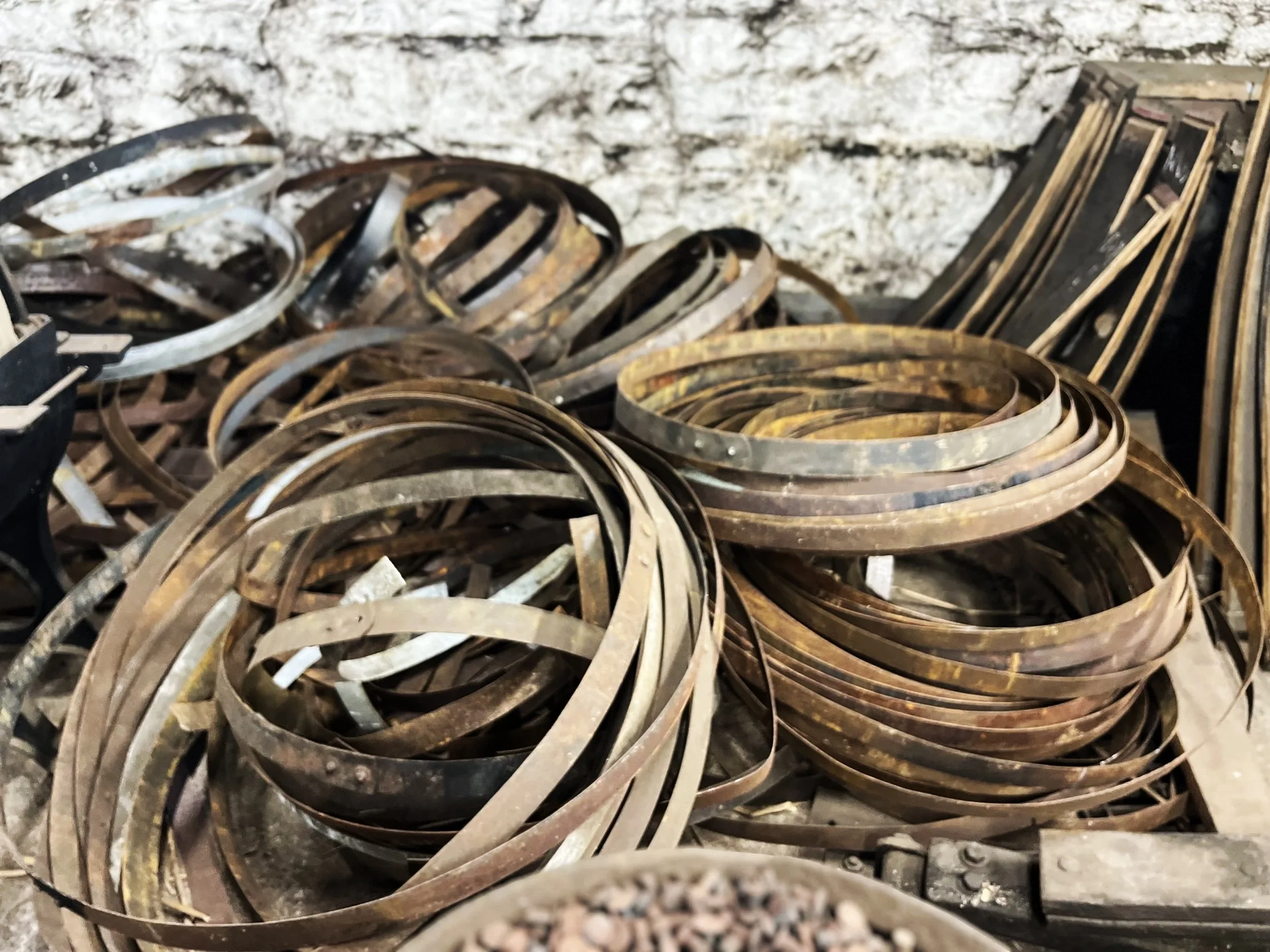 A pile of rusted metal hoops stacked together against a white brick wall.