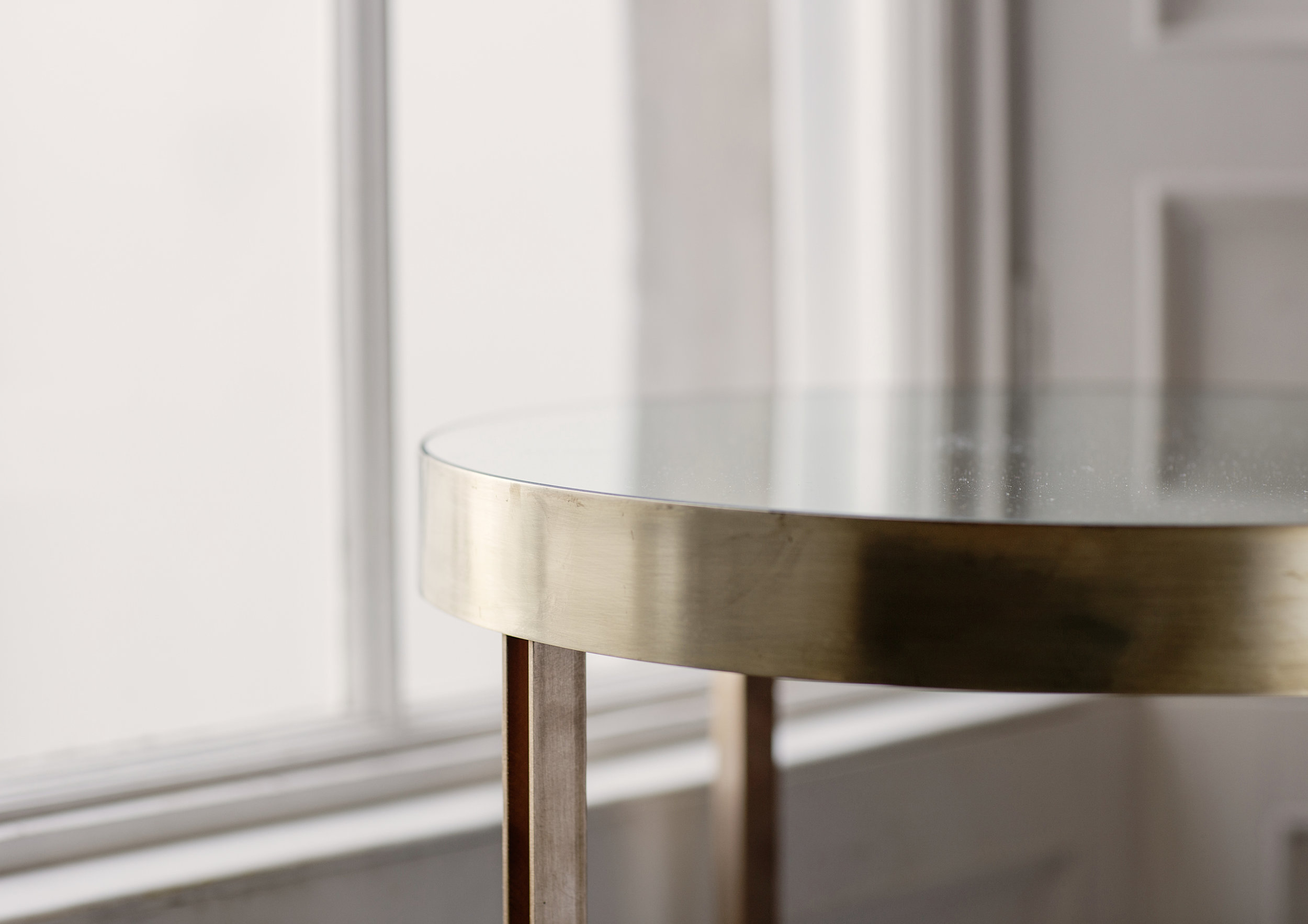 Close-up of a silver metallic round table with a smooth surface, situated indoors near a window.