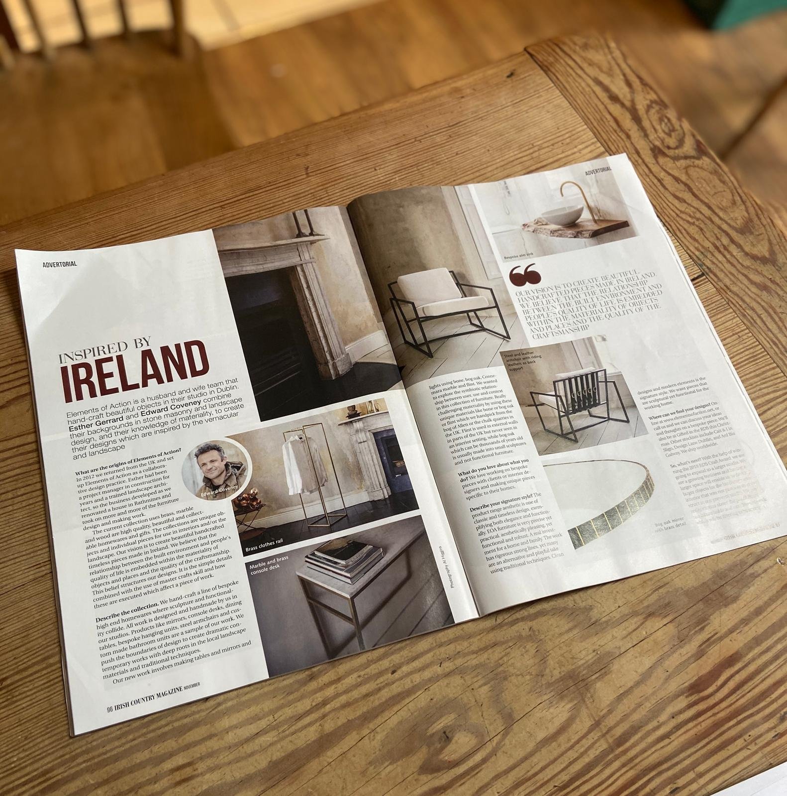 Open magazine on a wooden table featuring interior design and furniture, including a black metal armchair, white cushion, and various home decor items.