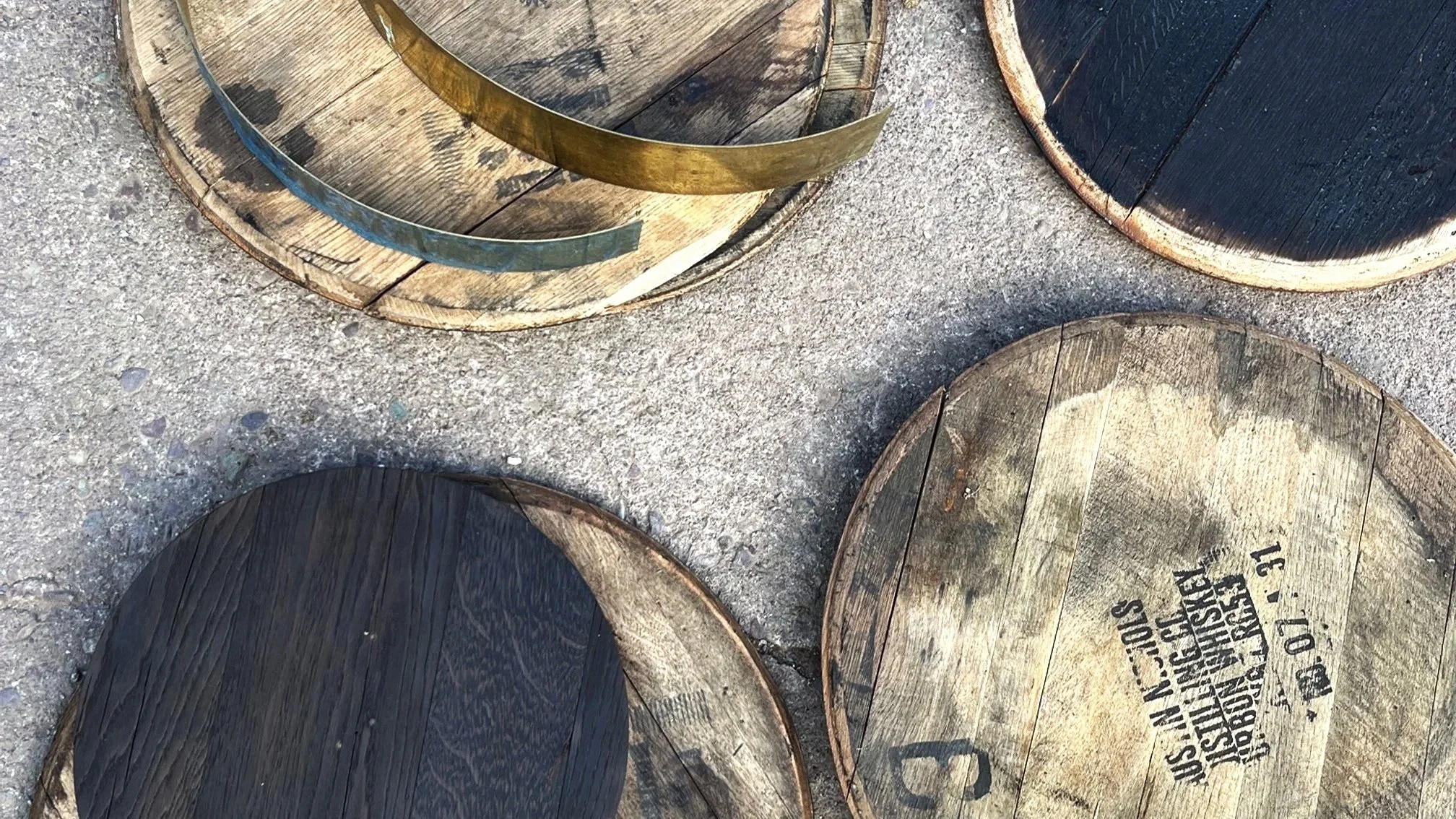 Close-up of several wooden barrels lying on a gravel surface, some with metal bands and one with printed text on the wood.