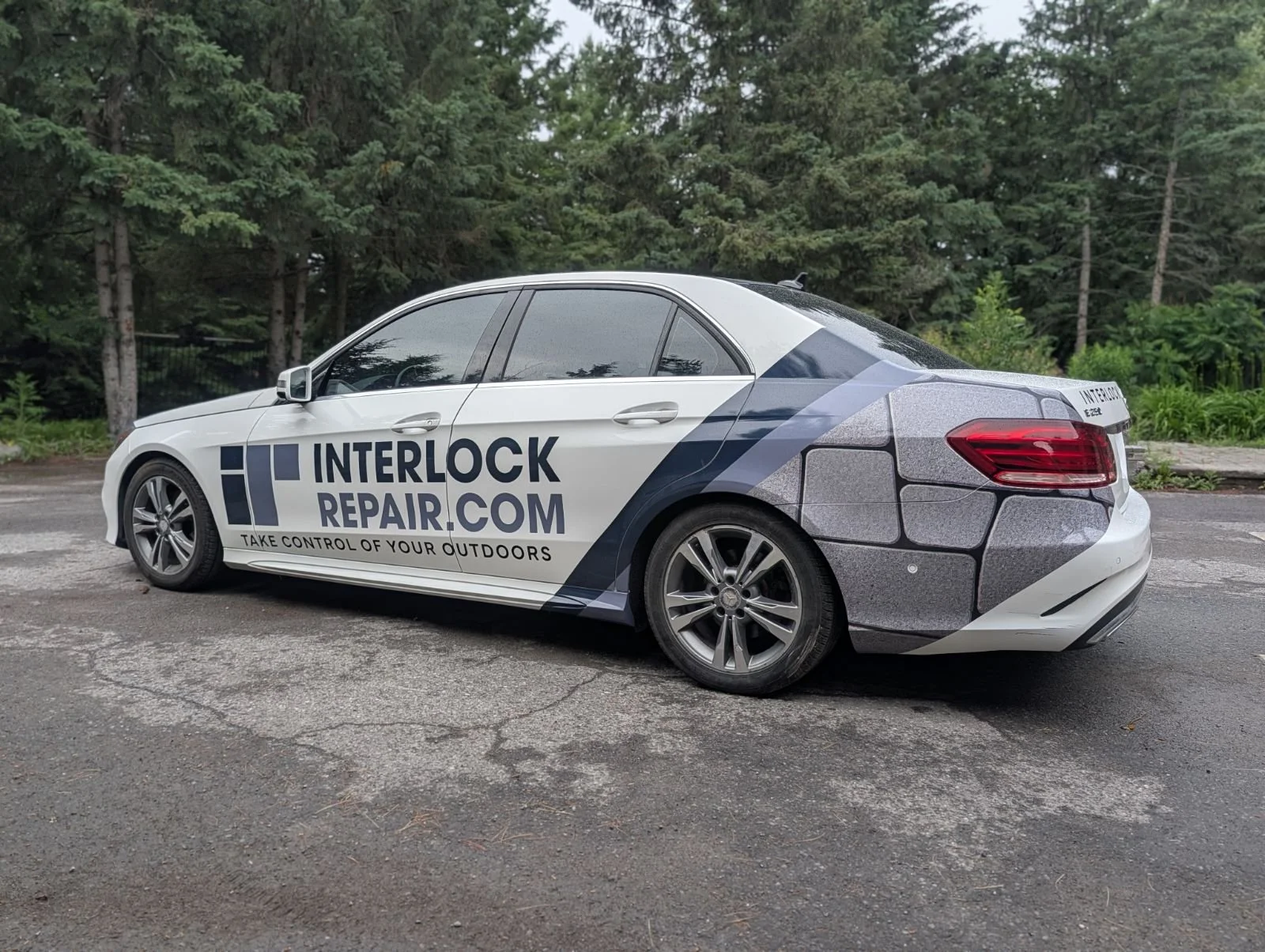 Custom partial vehicle wrap on a white sedan for Ottawa-based InterlockRepair.com, featuring bold lettering and a realistic stone paver vinyl graphic.