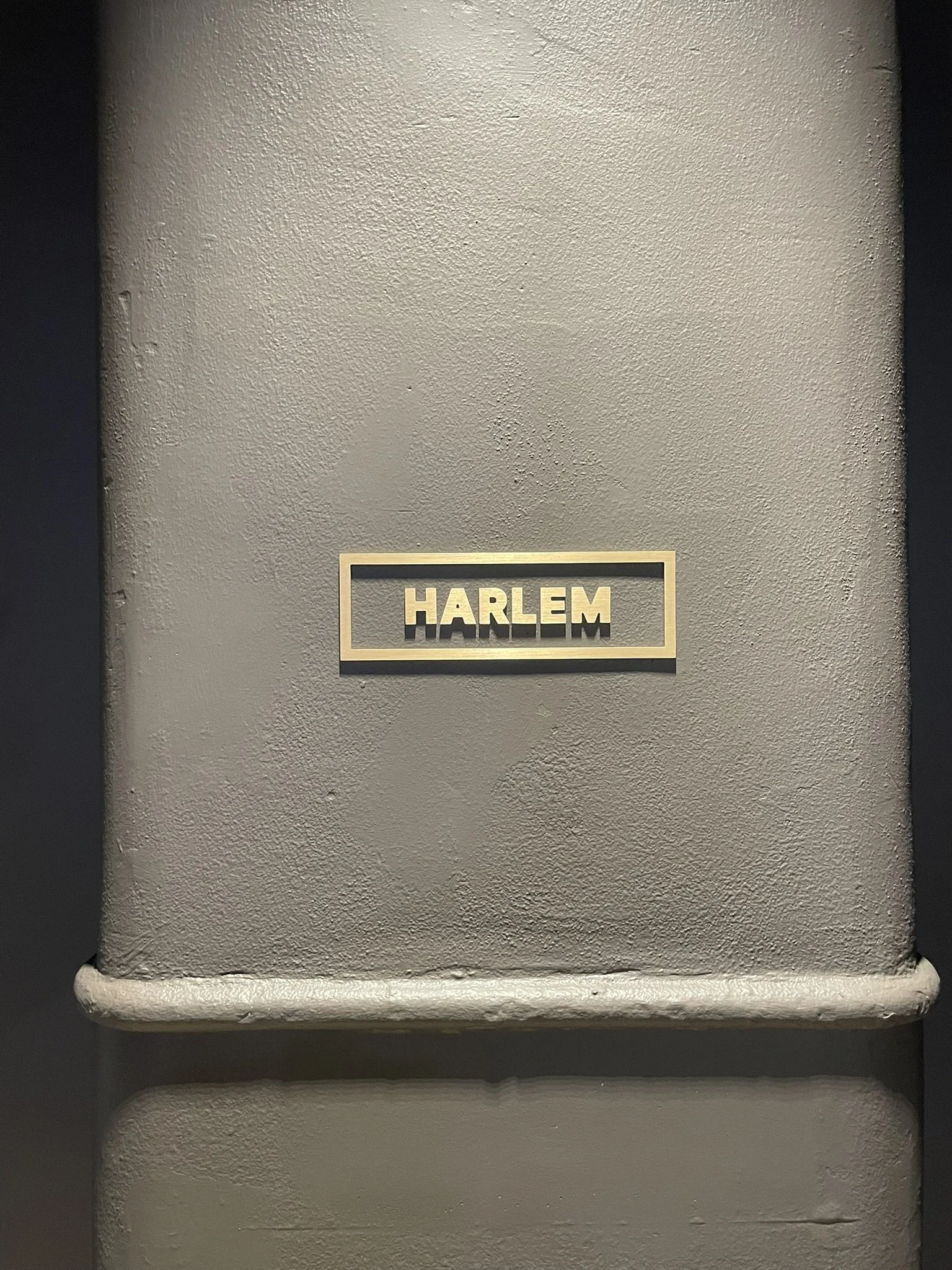 Gray wall with a gold-bordered sign reading 'HARLEM' in capital letters.
