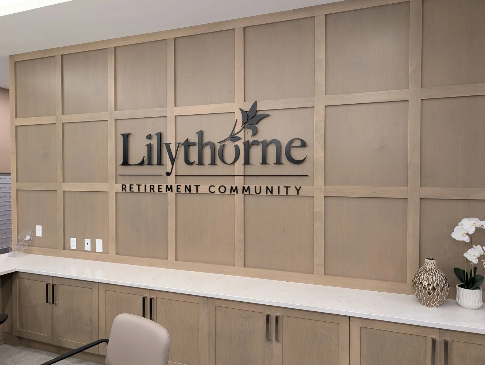 Interior of a retirement community with a wooden wall decor reading 'Lilythorne Retirement Community' and a decorative vase with flowers on a white countertop.