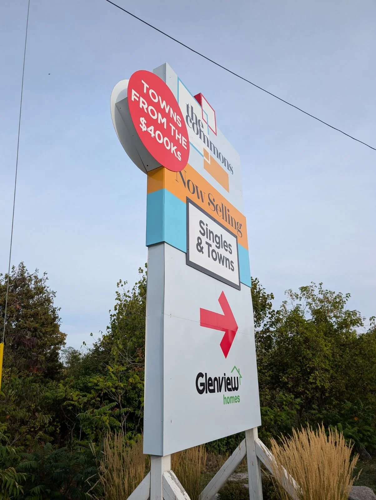 Signpost advertising Glenview homes with directions to Townhomes, now selling singles and towns, with a red arrow pointing right and a background of trees and a blue sky.