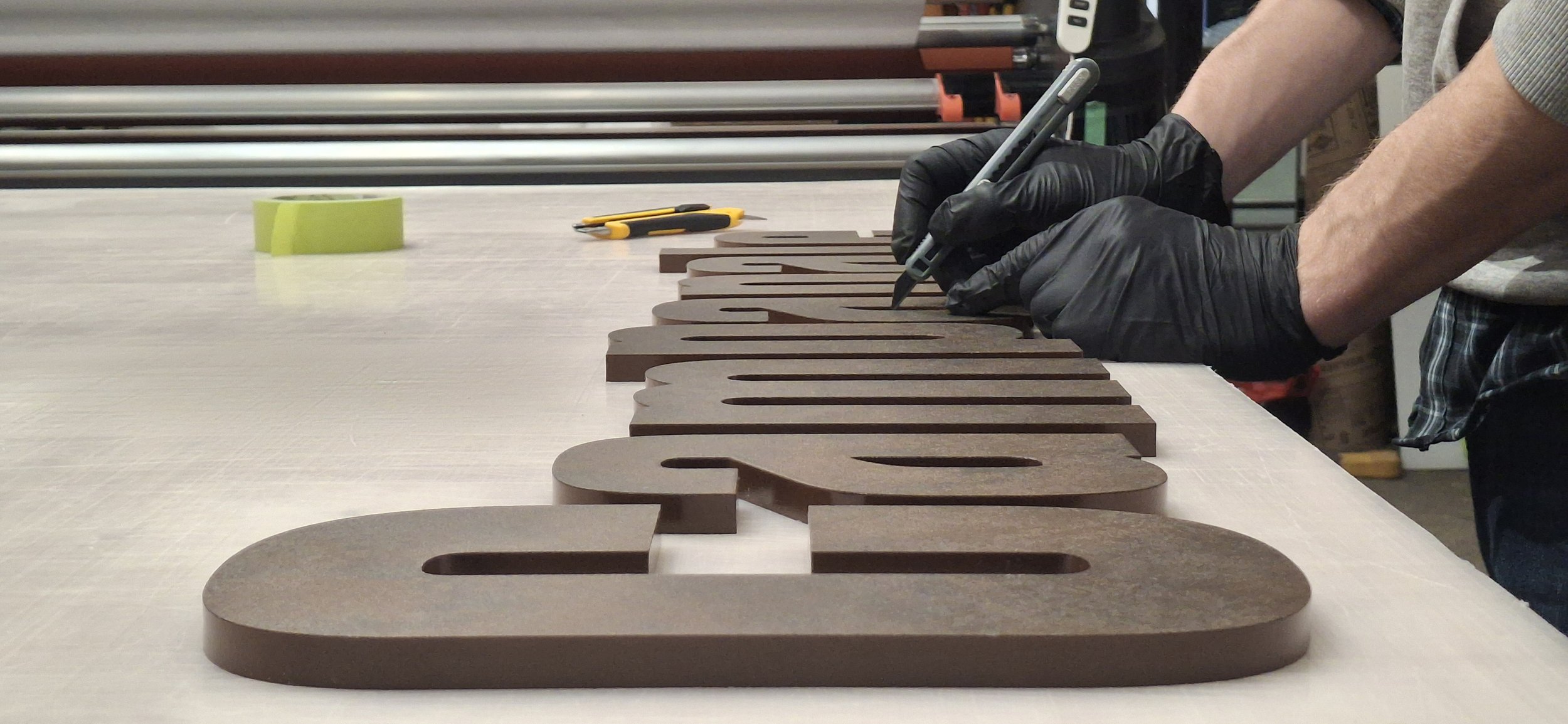 Close-up of an artisan wearing black gloves meticulously hand-detailing thick, custom dimensional lettering with a premium architectural finish in our Ottawa signage studio.