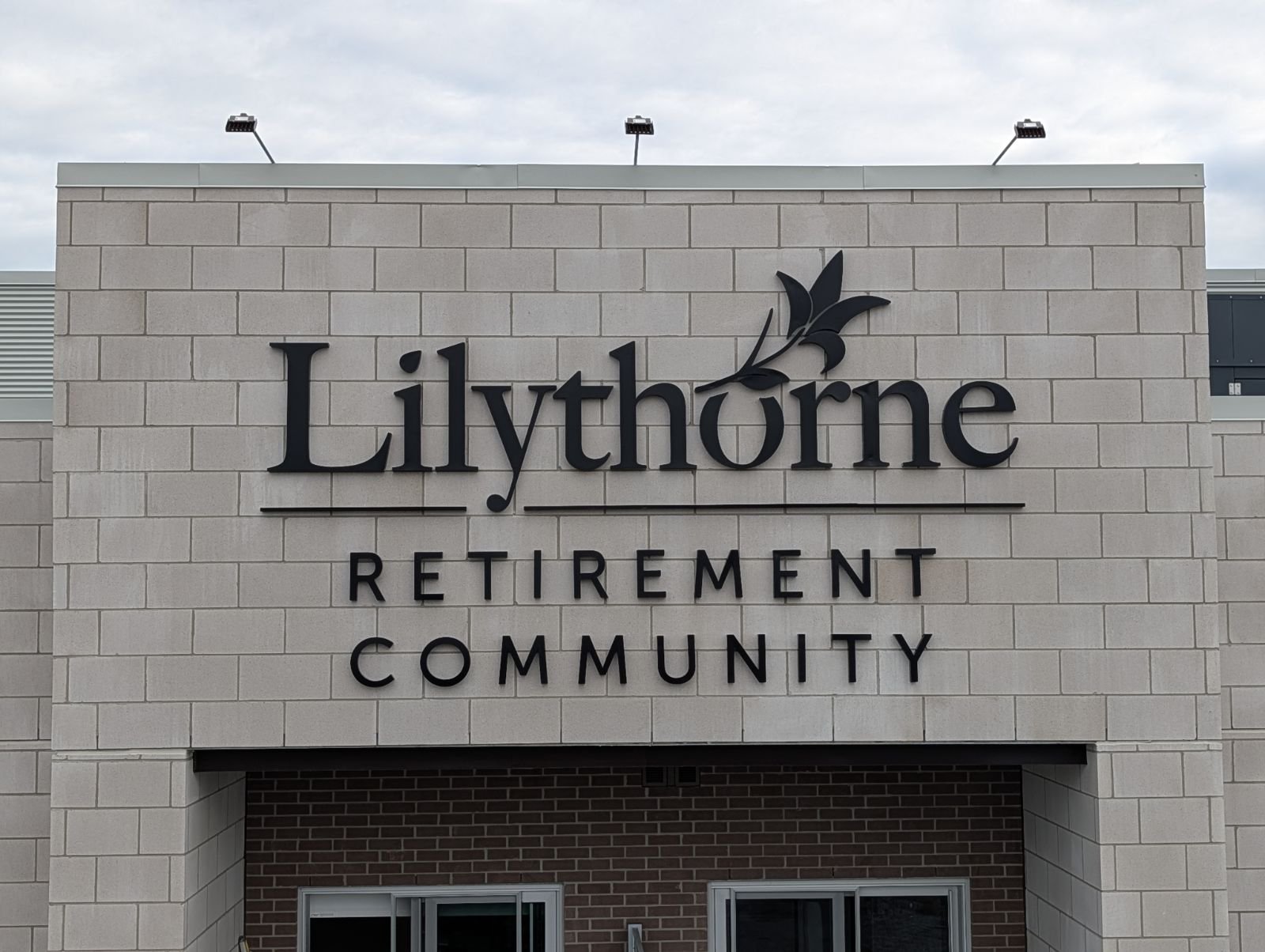 Sign reading 'Lilythorne Retirement Community' with a flower design in black on a beige brick building.
