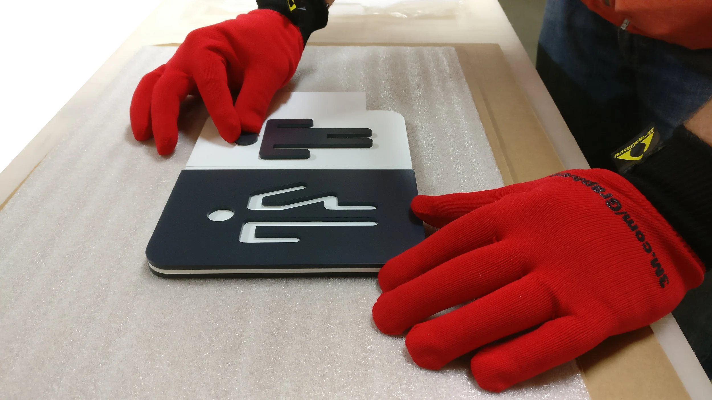 Person wearing red gloves arranges black and white sign letters on a surface.