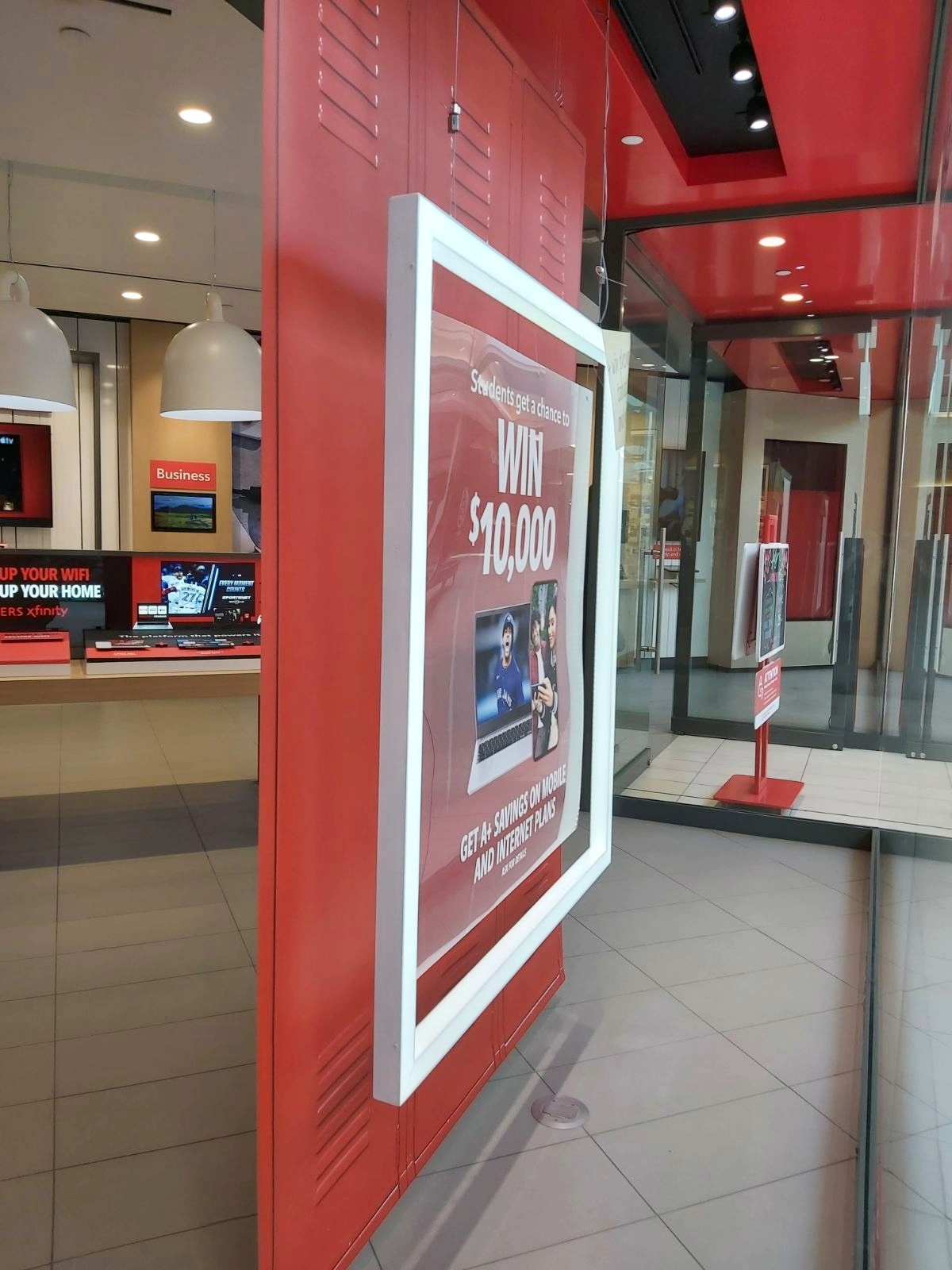 Promotional sign inside a shopping mall advertising a contest to win $10,000 for students, with a photo of two young women using a laptop and phone.