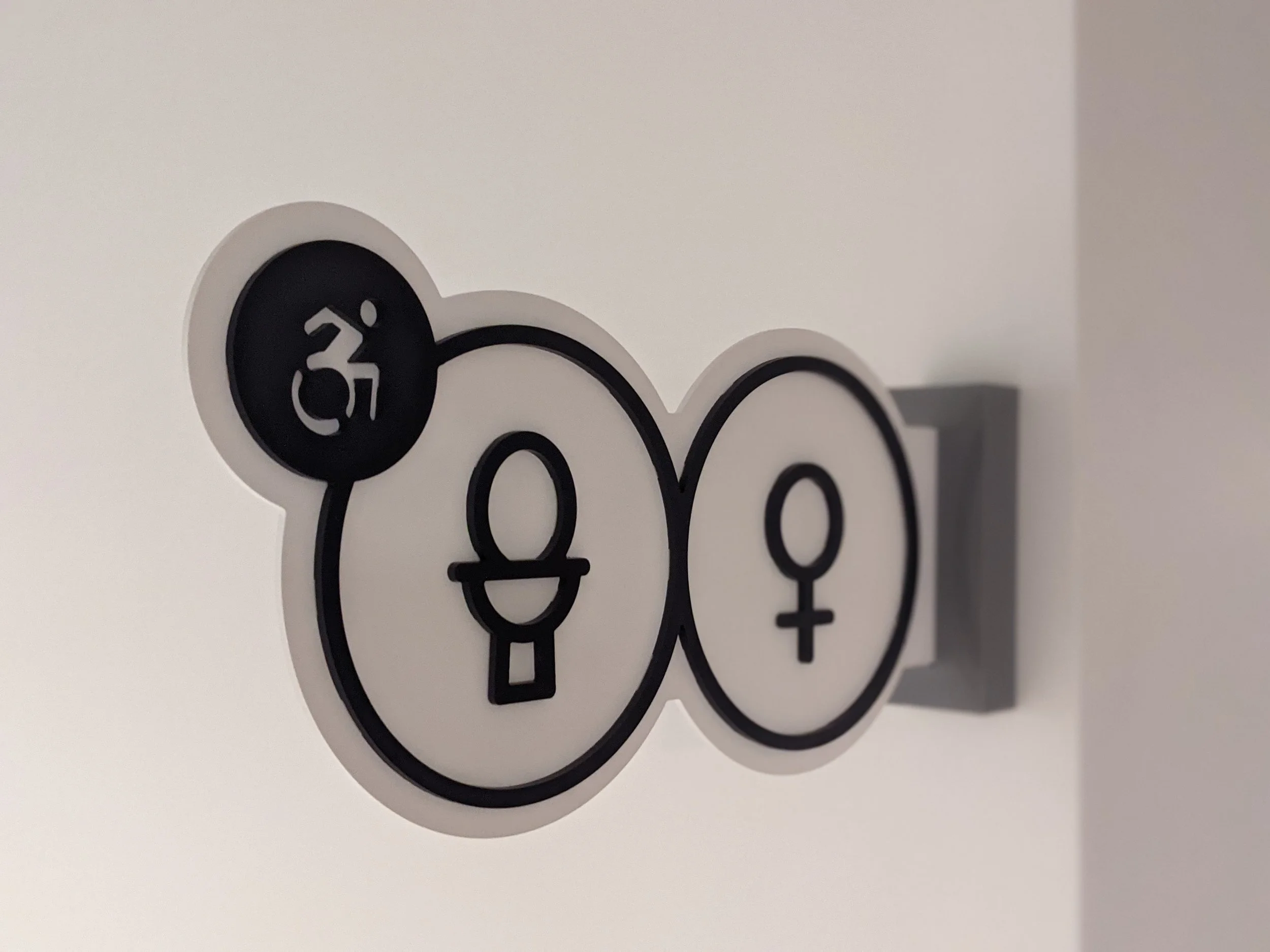 Close-up of a circular sign with gender symbols and a young woman figure, part of the word 'LOVE' on a white background.