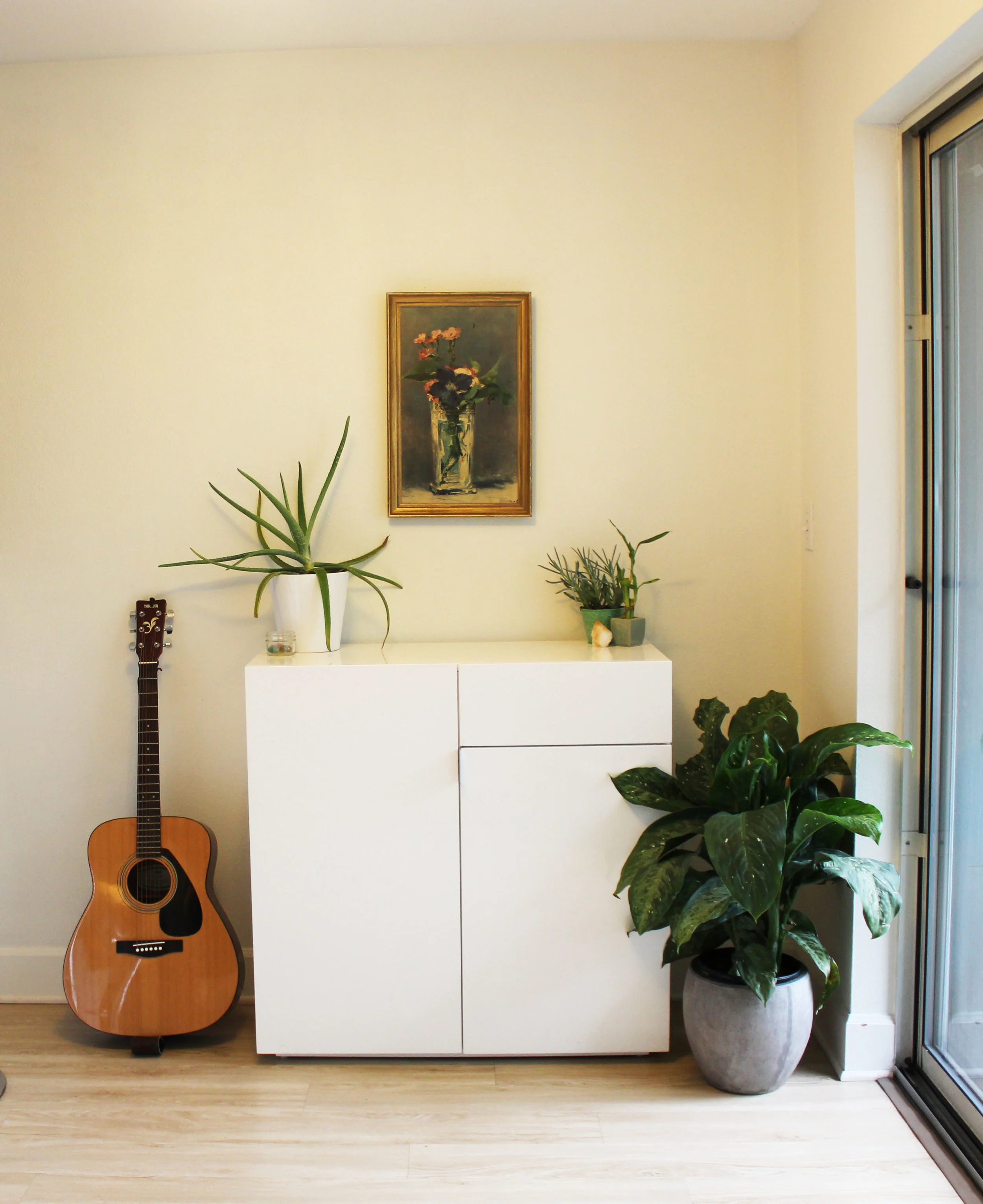 AFTER: Adding healthy plants represents a healthy flow of financial abundance. The guitar and thrifted artwork with a gold frame add a sense of warmth in the space. A few crystals that work to aid in attracting money (citrine, green aventurine and carnelian) sit on top of the bar, to represent her intention of attracting wealth into her life. 