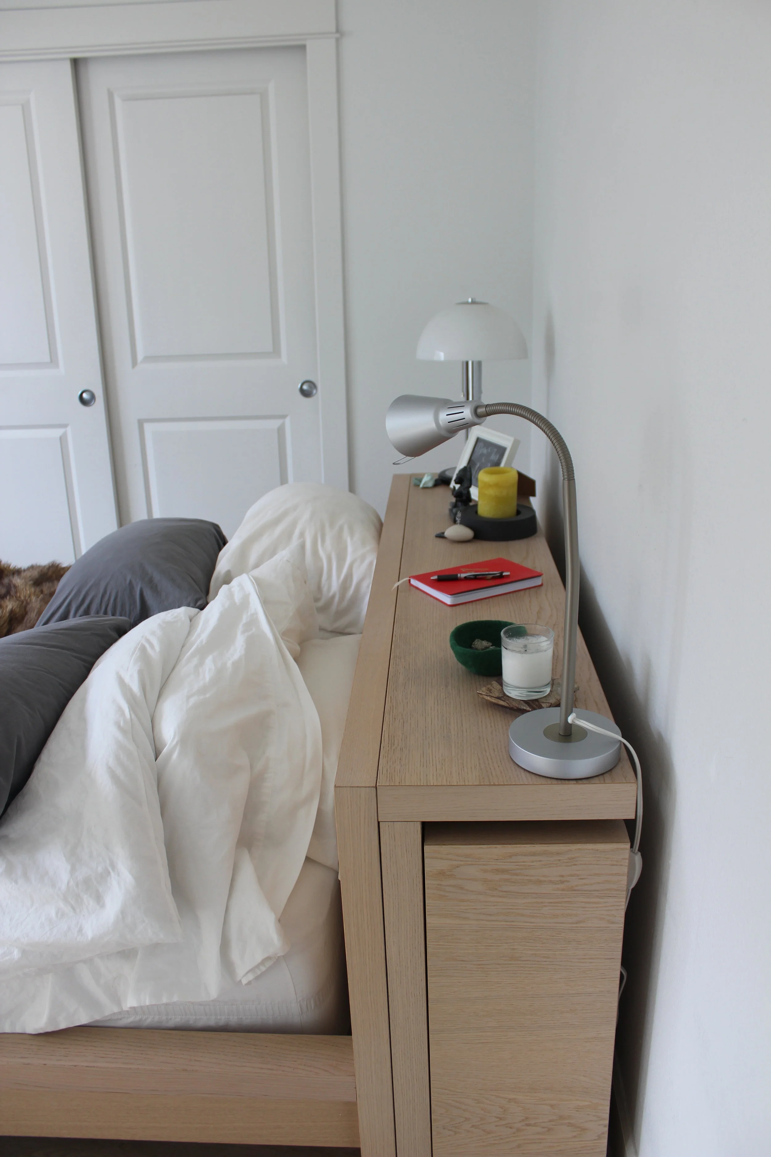 BEFORE: Blank walls and clutter on the headboard makes the space feel transitional and messy. The mismatched lamps feel out of place in contrast to warm wood tones in the bedroom, and the lack of art is uninspiring. 