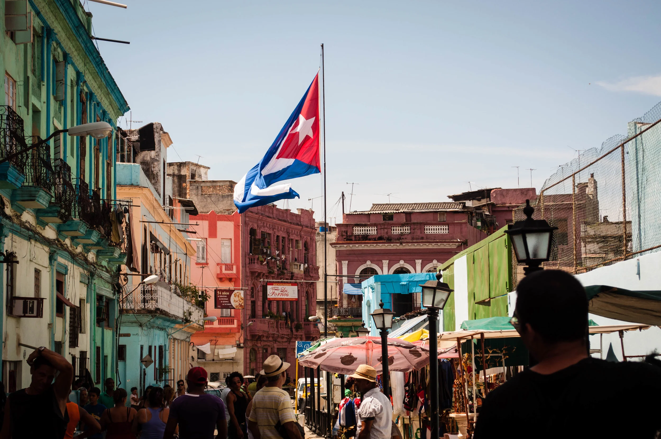 Giant Cuban flag in a large busy avenue with tourist surrounded by colourful buildings. This scene was seen during our day trip to La Havana