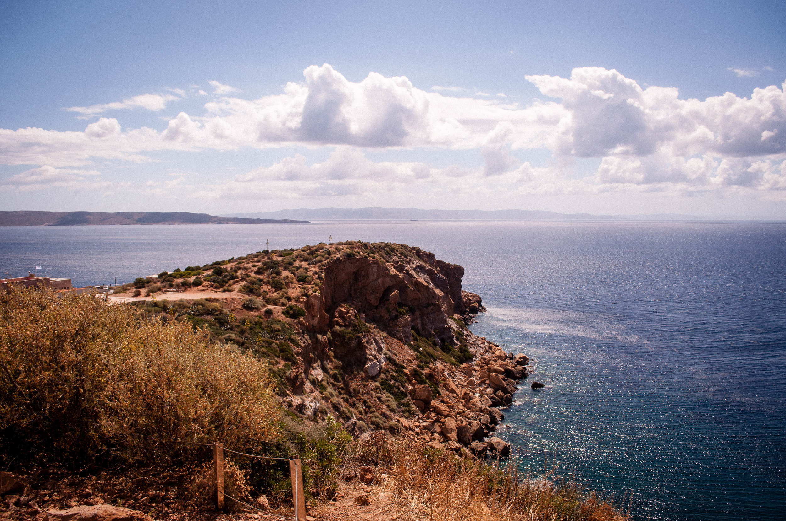 Blue sky with clouds, sea and creeks with desert-like vegetation in Sounion (Greece) 