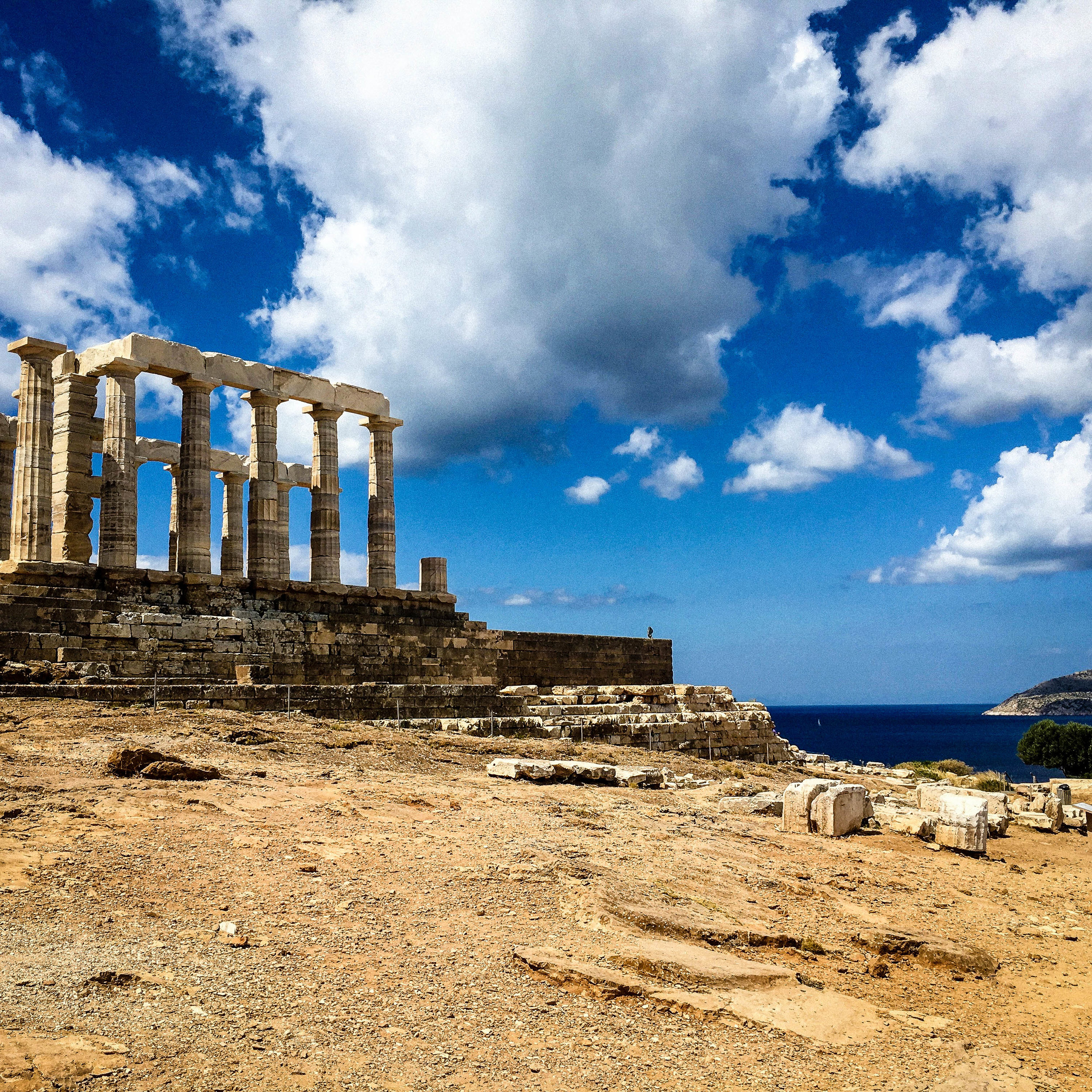 Blue sky with clouds, and the remaining ruins of the temple of Sounion. This image is a good representation for the article “how to avoid tourists in Greece” 