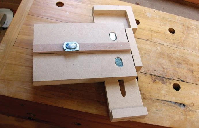 Two T bolt heads in slots hold the sliding mechanism in place. Small feet on either end act as stops and support the wood being cut.