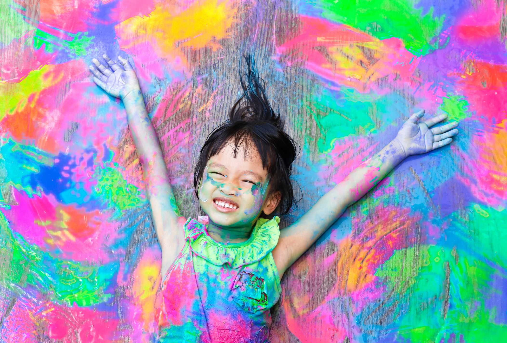Smiling child covered in colorful paint with arms raised, celebrating creative expression and joyful learning