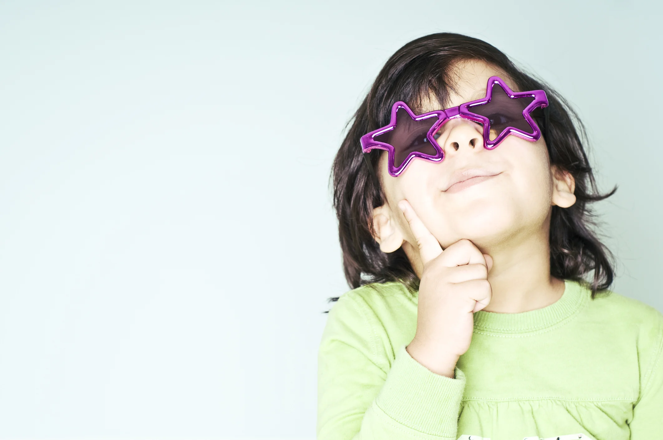 Child wearing star-shaped sunglasses and smiling thoughtfully, representing individuality and confidence in a supportive childcare setting