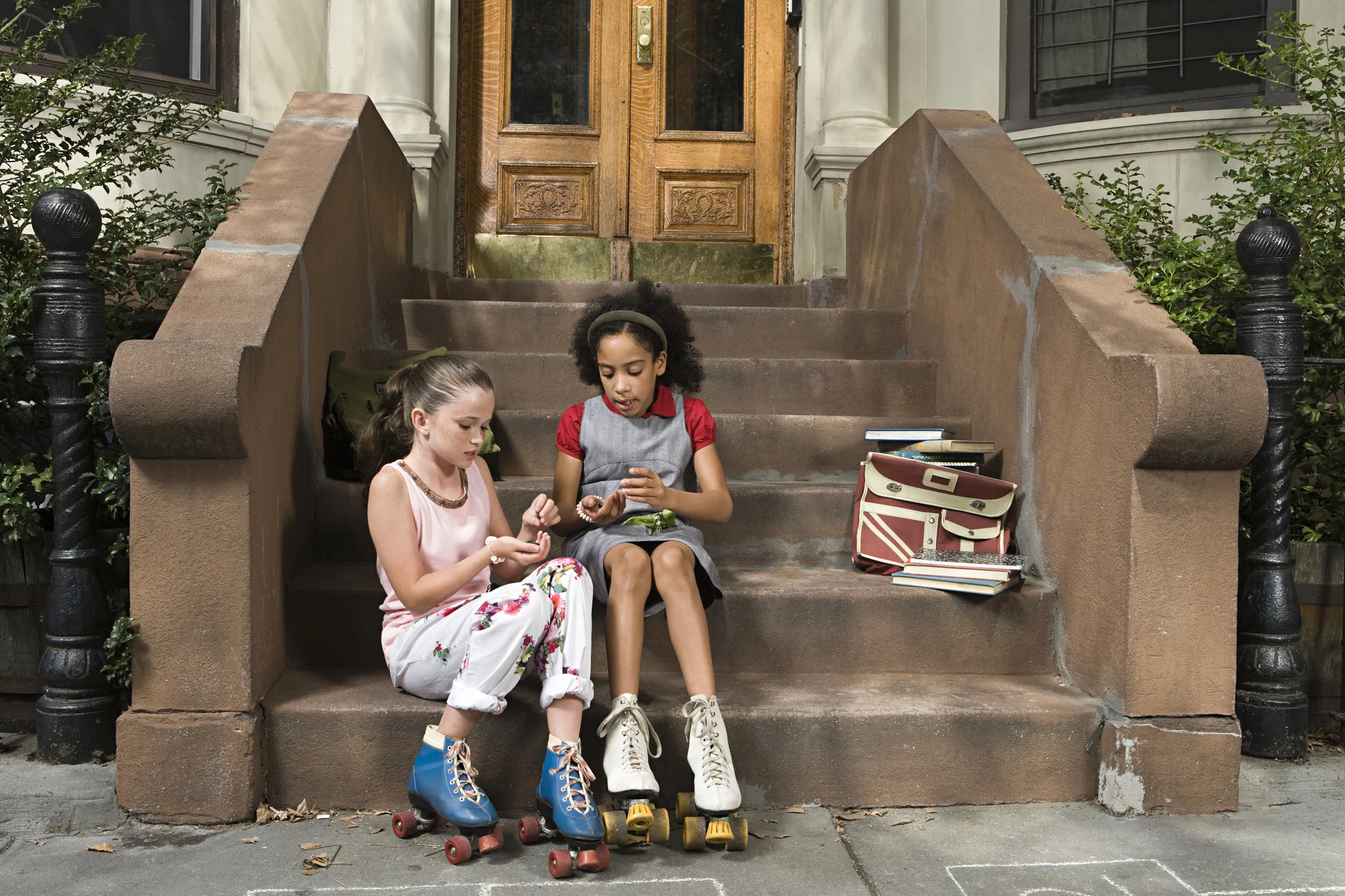 Two children sitting on front steps wearing roller skates and sharing a quiet moment together after school, with books beside them.