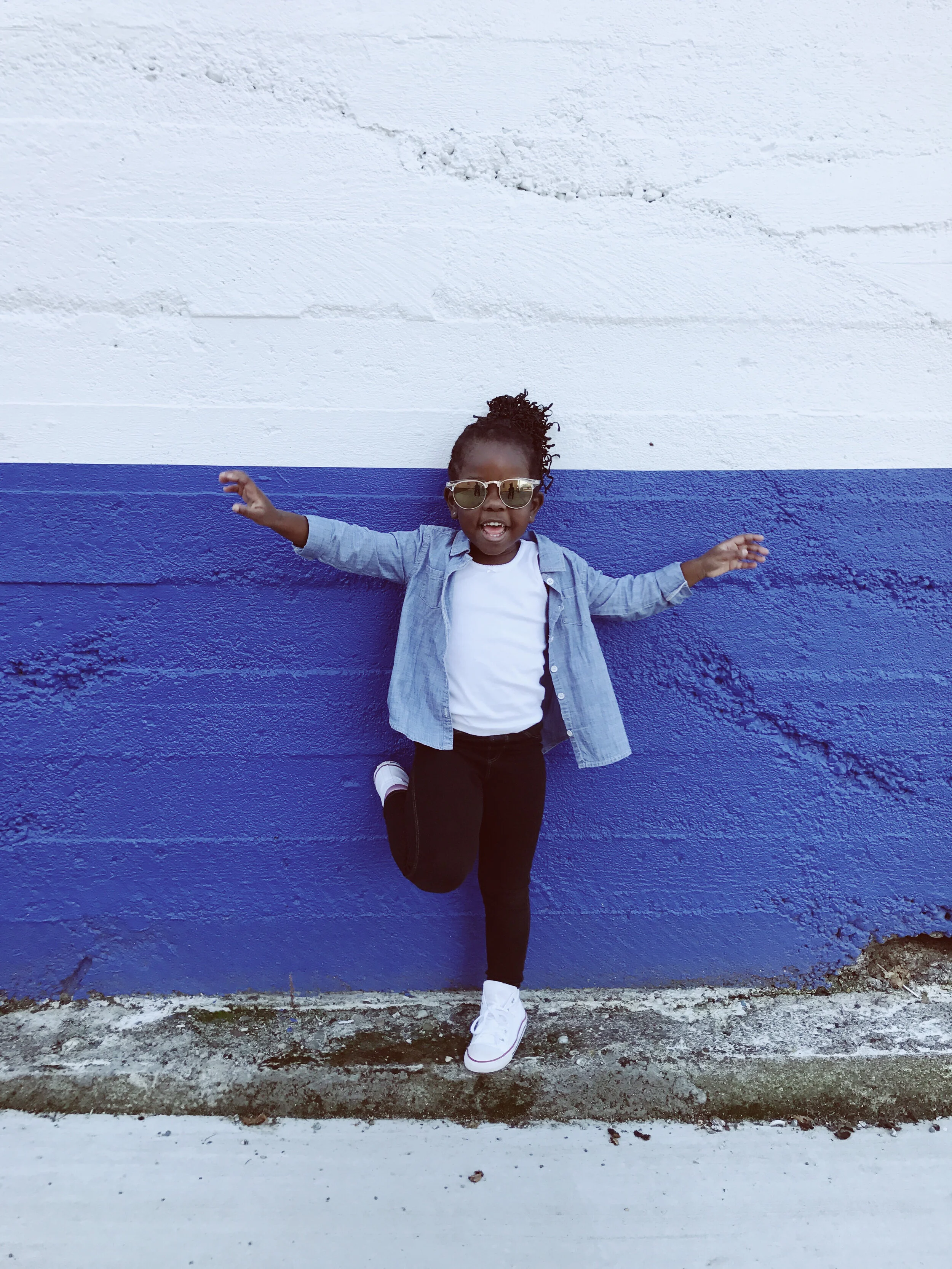 Confident child wearing sunglasses and smiling while standing against a blue wall, expressing individuality and joy in a supportive environment