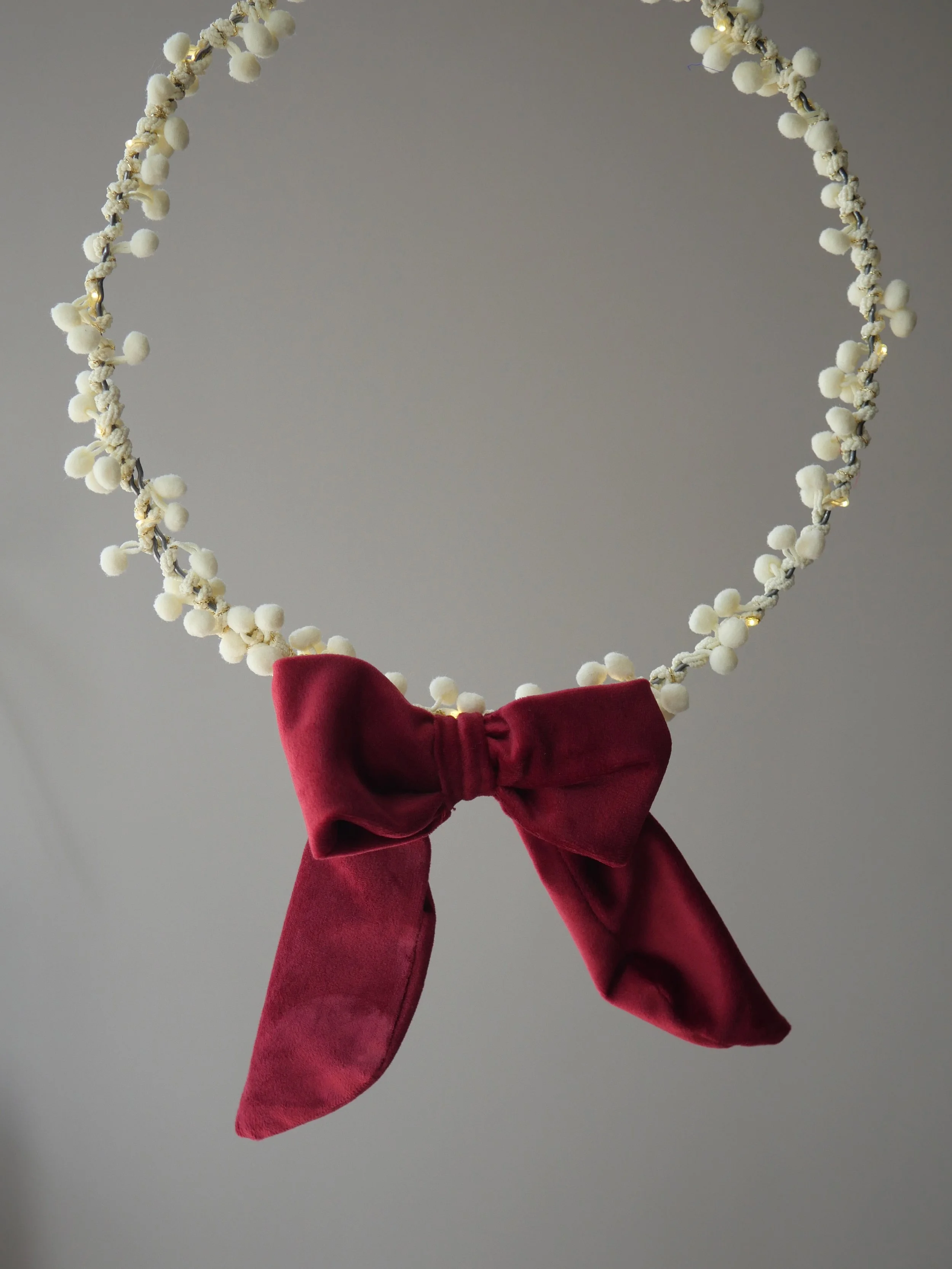 Red velvet battery pack cover bow displayed on cream pom pom fairy lights