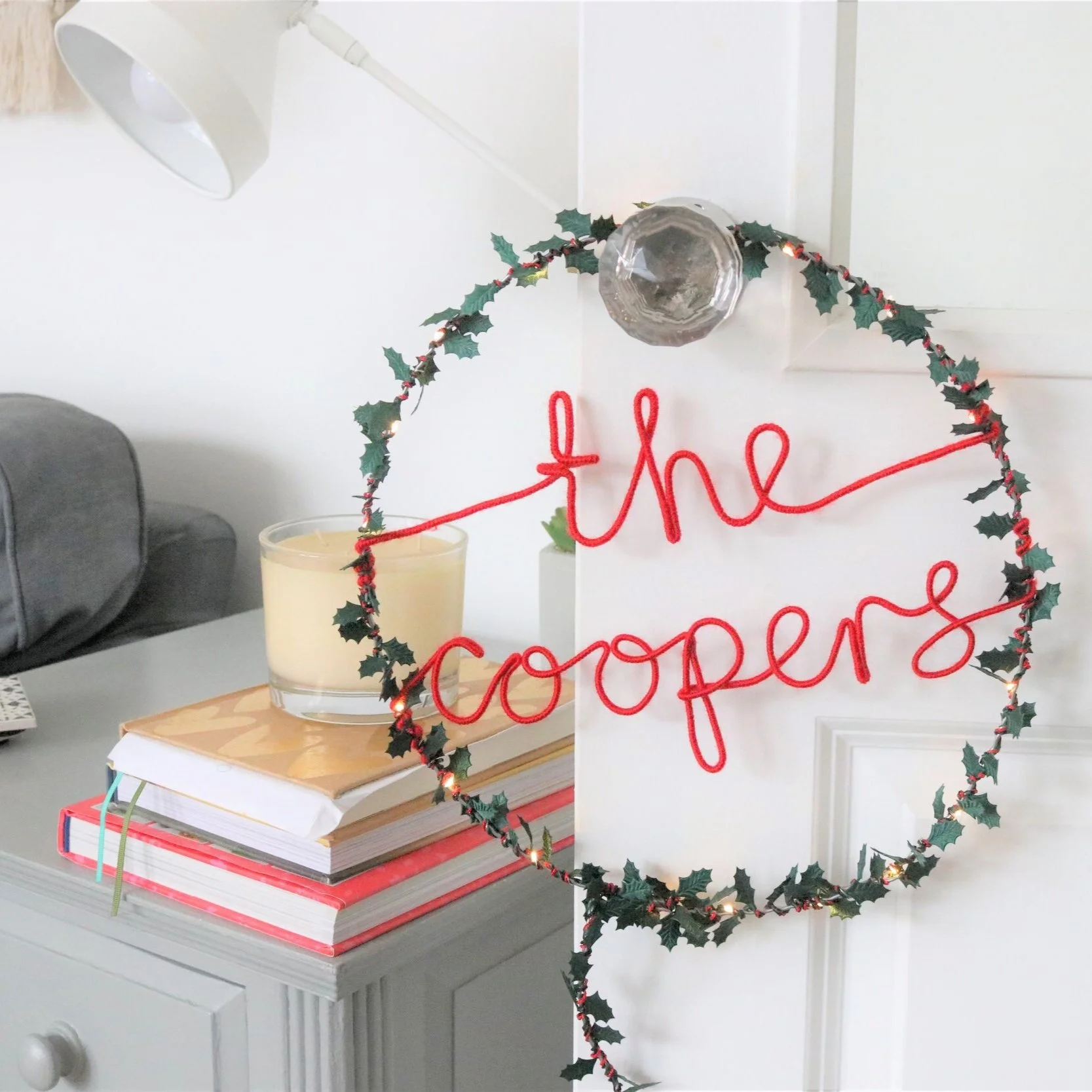 Personalised surname in red writing fairy light hoop with holly leave hanging off white living room door.