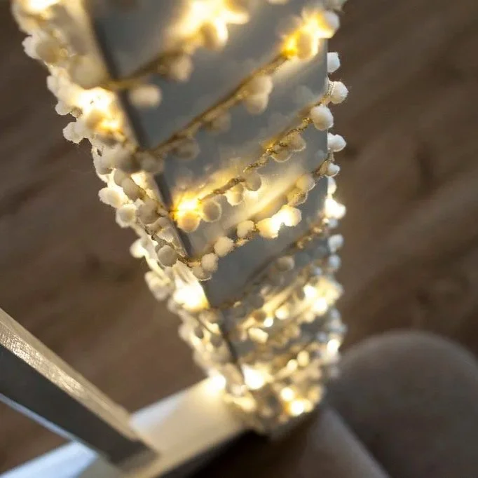 Warm white pom pom fairy lights wrapped around a wooden staircase banister.