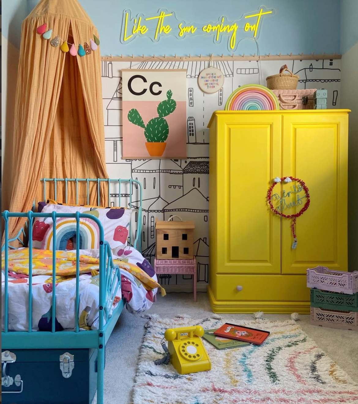 Colourful children's bedroom with a bright yellow wardrobe, turquoise metal bed, patterned bedding and a yellow illuminated wall sign.