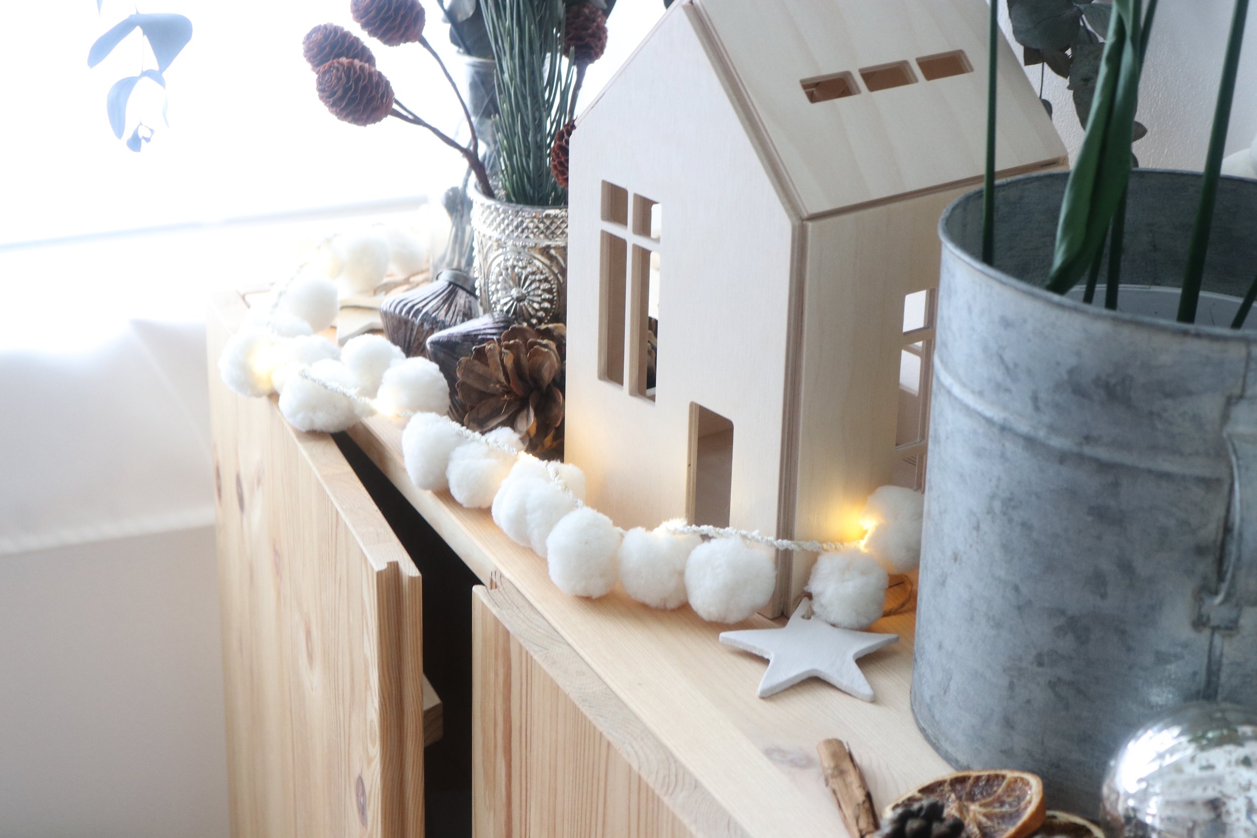 White pom pom fairy lights styled with a wooden house and festive decorations