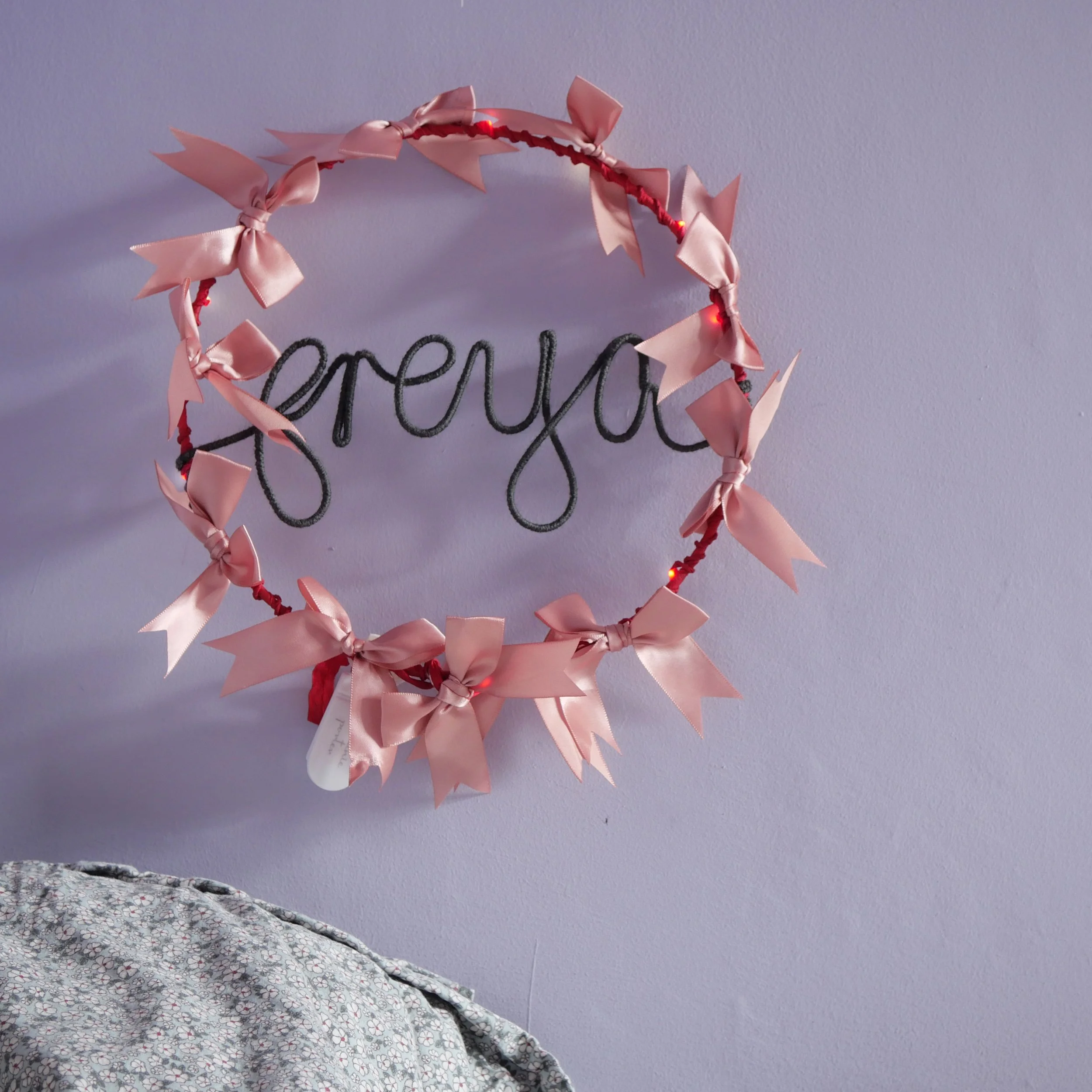 5  Freya personalised name light with pink satin bows displayed on a lavender bedroom wall above floral bedding.