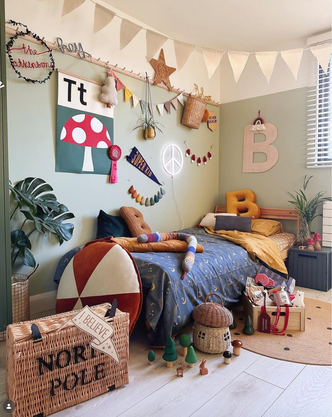 Children's bedroom with sage green walls, patterned bedding, bunting, colourful artwork, handmade decorations and a personalised Christmas fairy light wreath.
