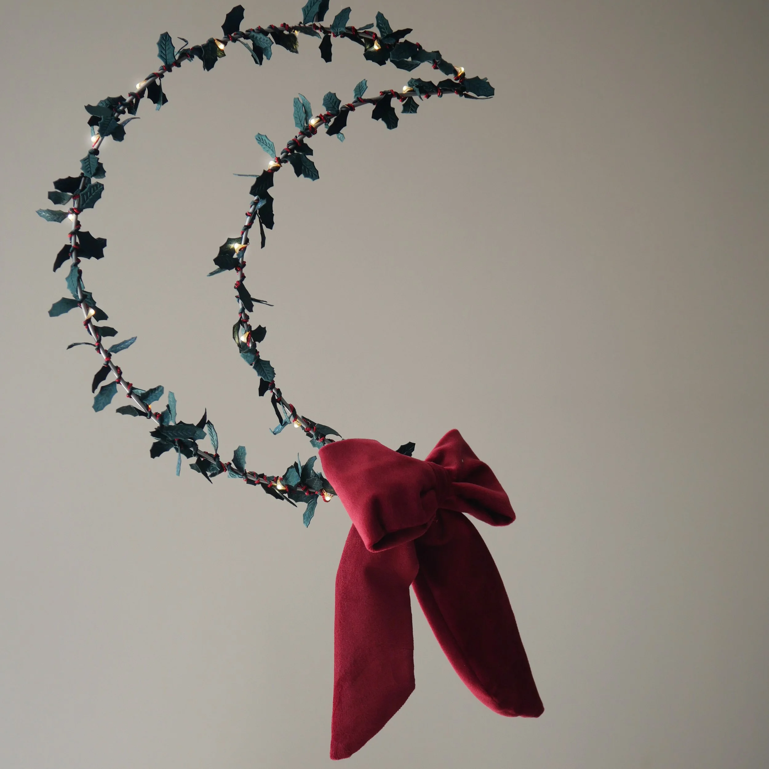 Handmade holly fairy light wreath with warm white LEDs, finished with an oversized red velvet bow.