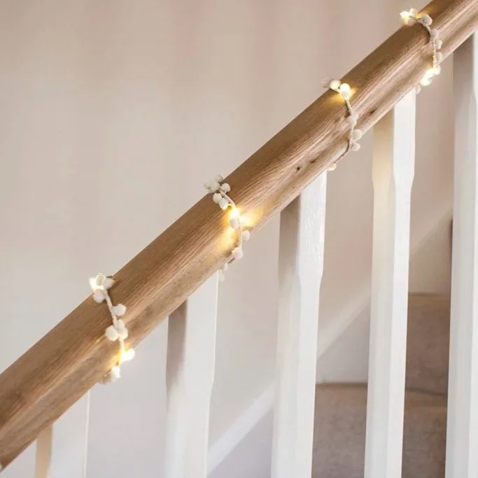 Close-up of warm white pom pom fairy lights draped along a wooden stair handrail.