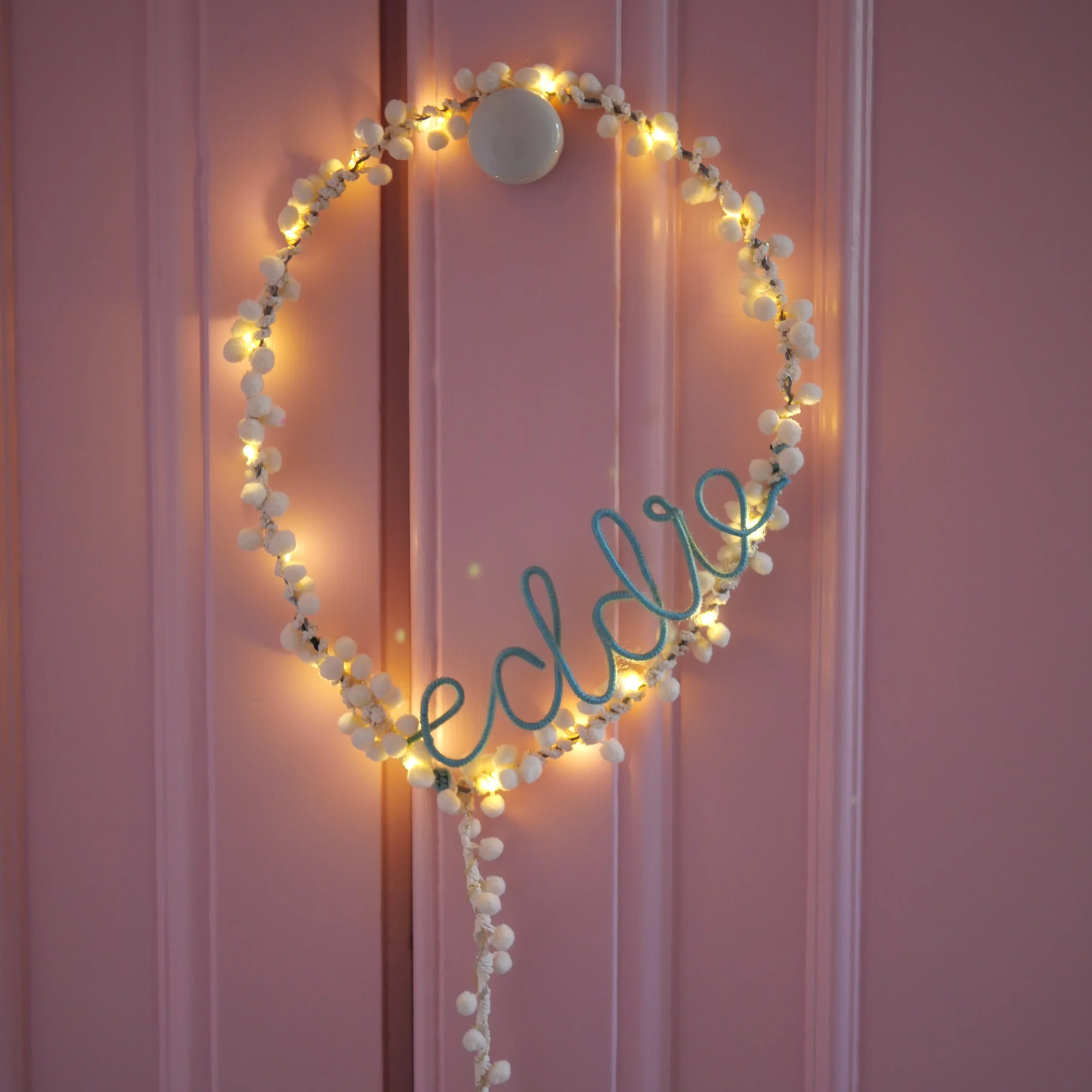 Soft white personalised balloon light glowing on a pink door