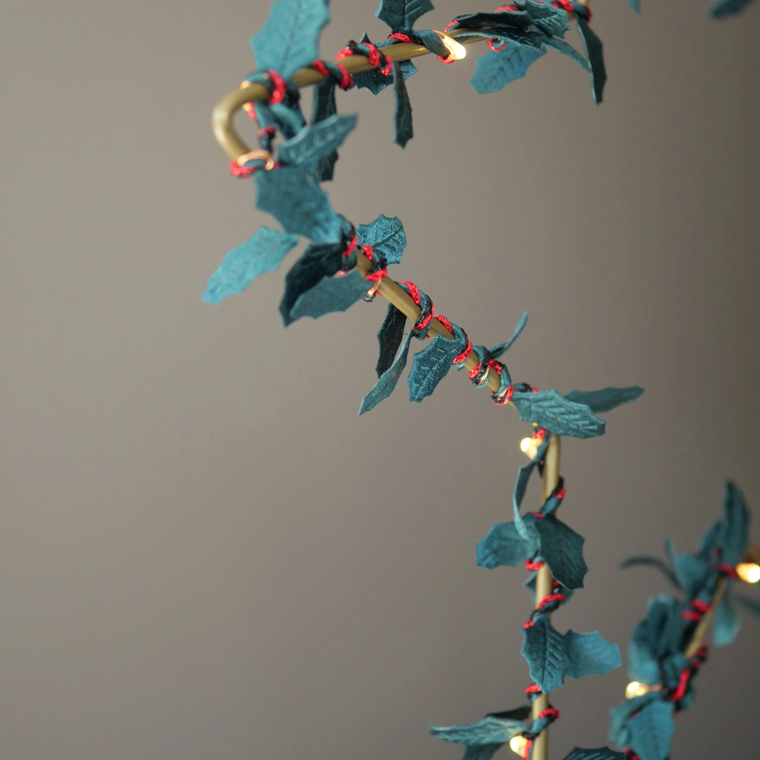 Close-up of handmade green holly and berry fairy lights wrapped around a gold metal wreath with warm white LEDs.