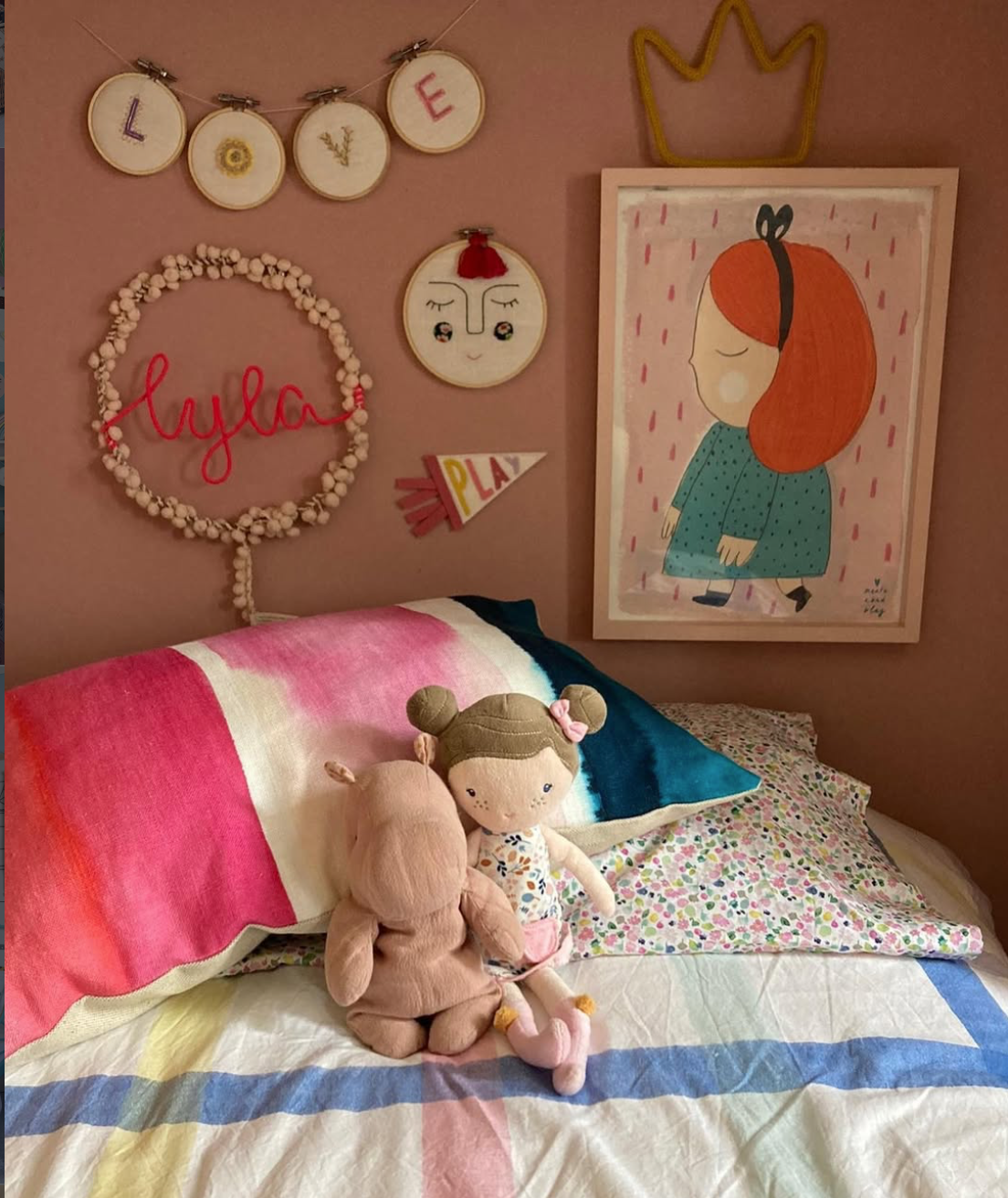 Pink children's bedroom with colourful striped bedding, framed artwork, handmade wall decorations and a personalised Lyla fairy light wreath.