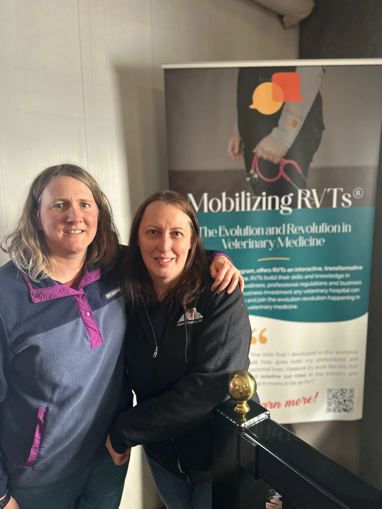 Nicole and Ingrid standing together with a standing banner for the Mobilizing RVTs program hosted by BS Communications