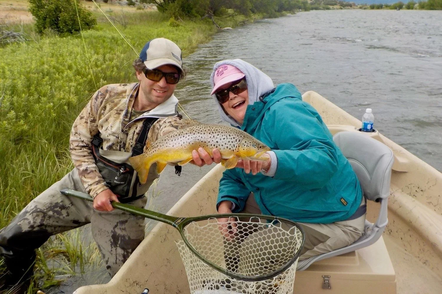 A female angler leaning in to see a beautiful brown trout held by David Kern on a Madison River guided fly fishing trip.