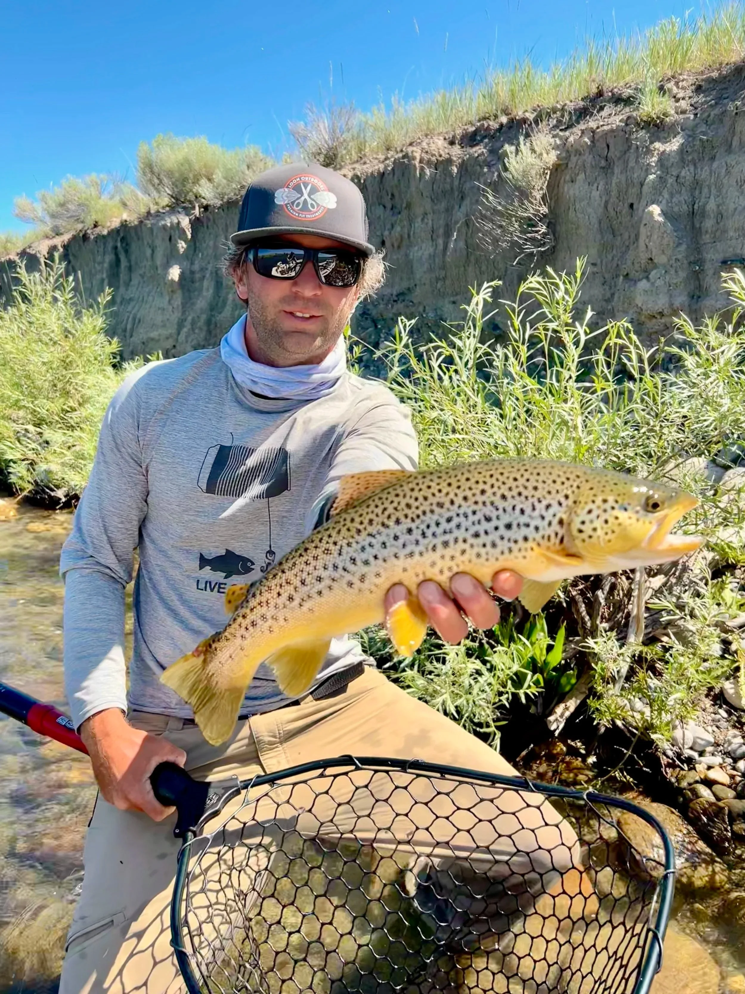 A Flyshot Outfitters guide holding a large brown trout on the Upper Missouri River near Townsend, Montana, known for its trophy-sized migratory fish and beautiful river braids.