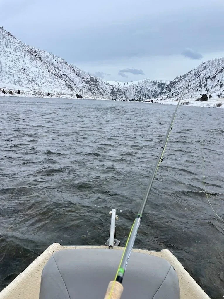 A peaceful winter landscape on the Lower Madison River after a fresh snowfall, featuring an Orvis fly rod in a drift boat during a guided Montana fly fishing trip near Bozeman.