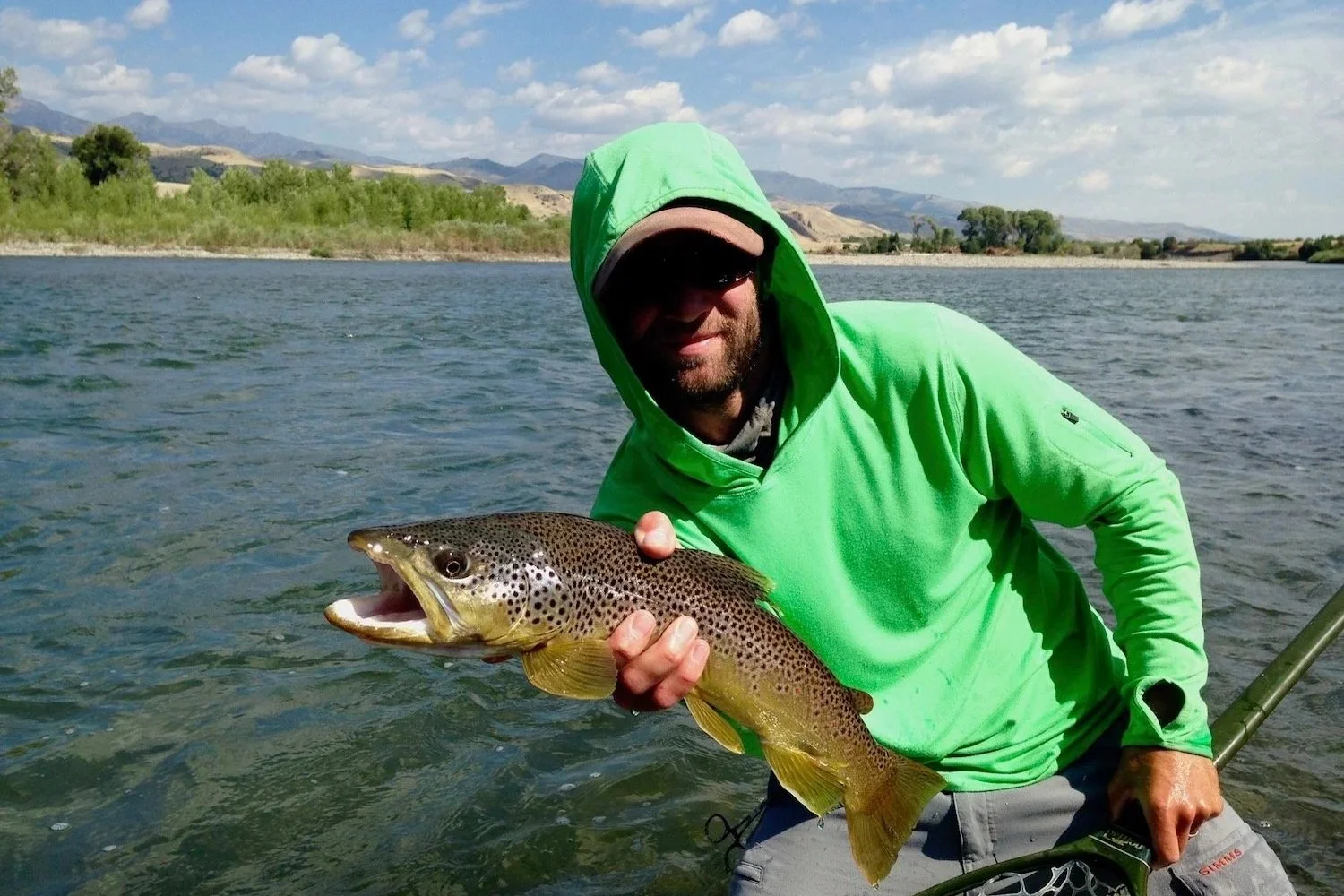 Flyshot Outfitters owner and guide David Kern holding a wild Yellowstone River brown trout with the stunning Gallatin Range mountains in the background during a guided fly fishing trip near Livingston, Montana.
