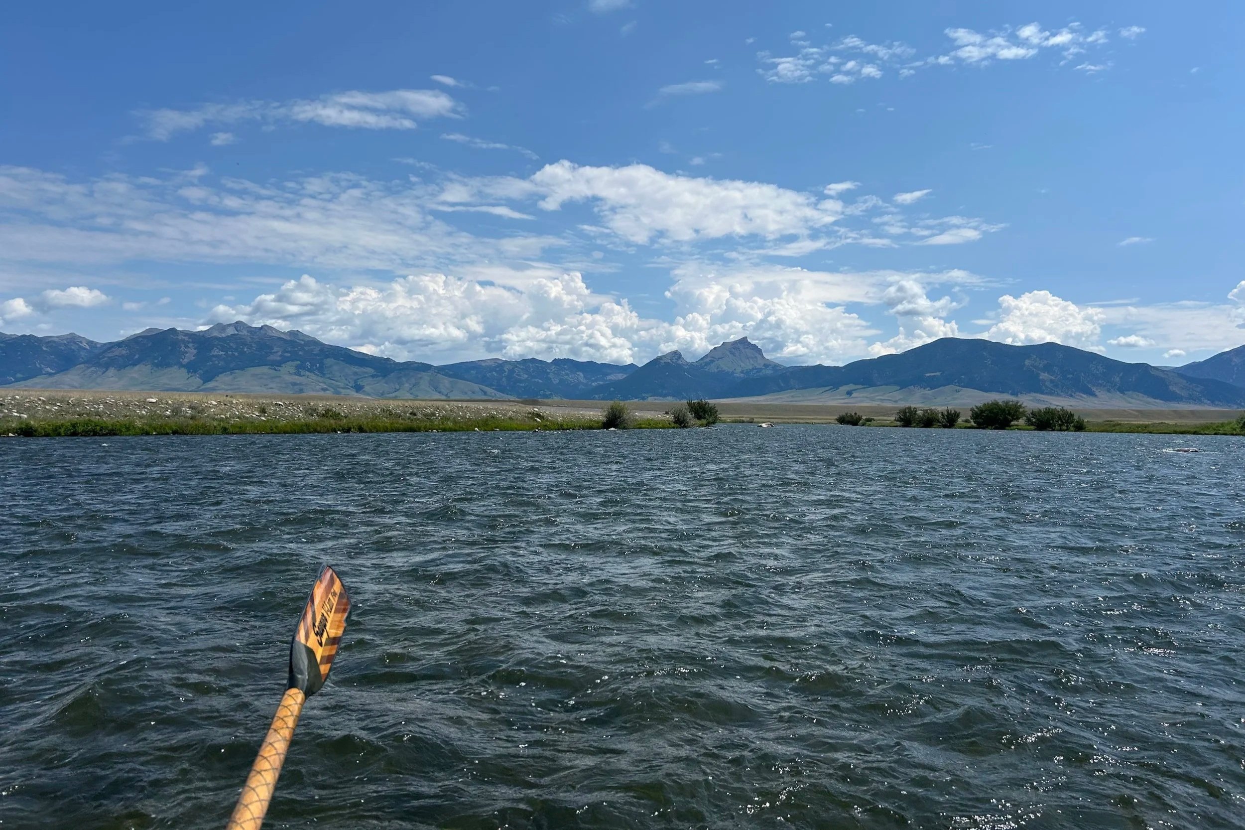The Madison Range mountains towering under a bluebird sky and large white clouds during a summer float trip.