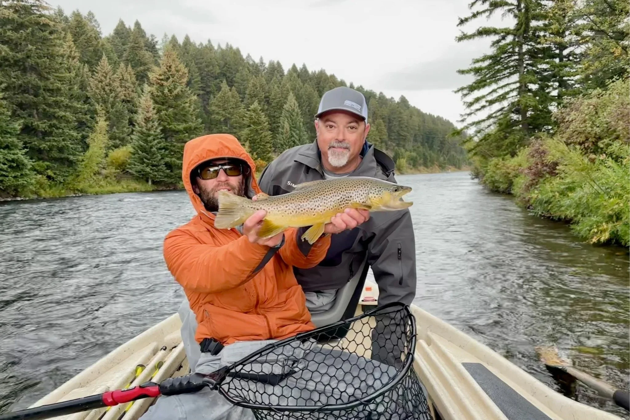 Flyshot Outfitters guide David Kern showcasing a trophy-sized brown trout for a smiling client during a premier full-day drift boat trip on the Madison River near Bozeman, Montana.