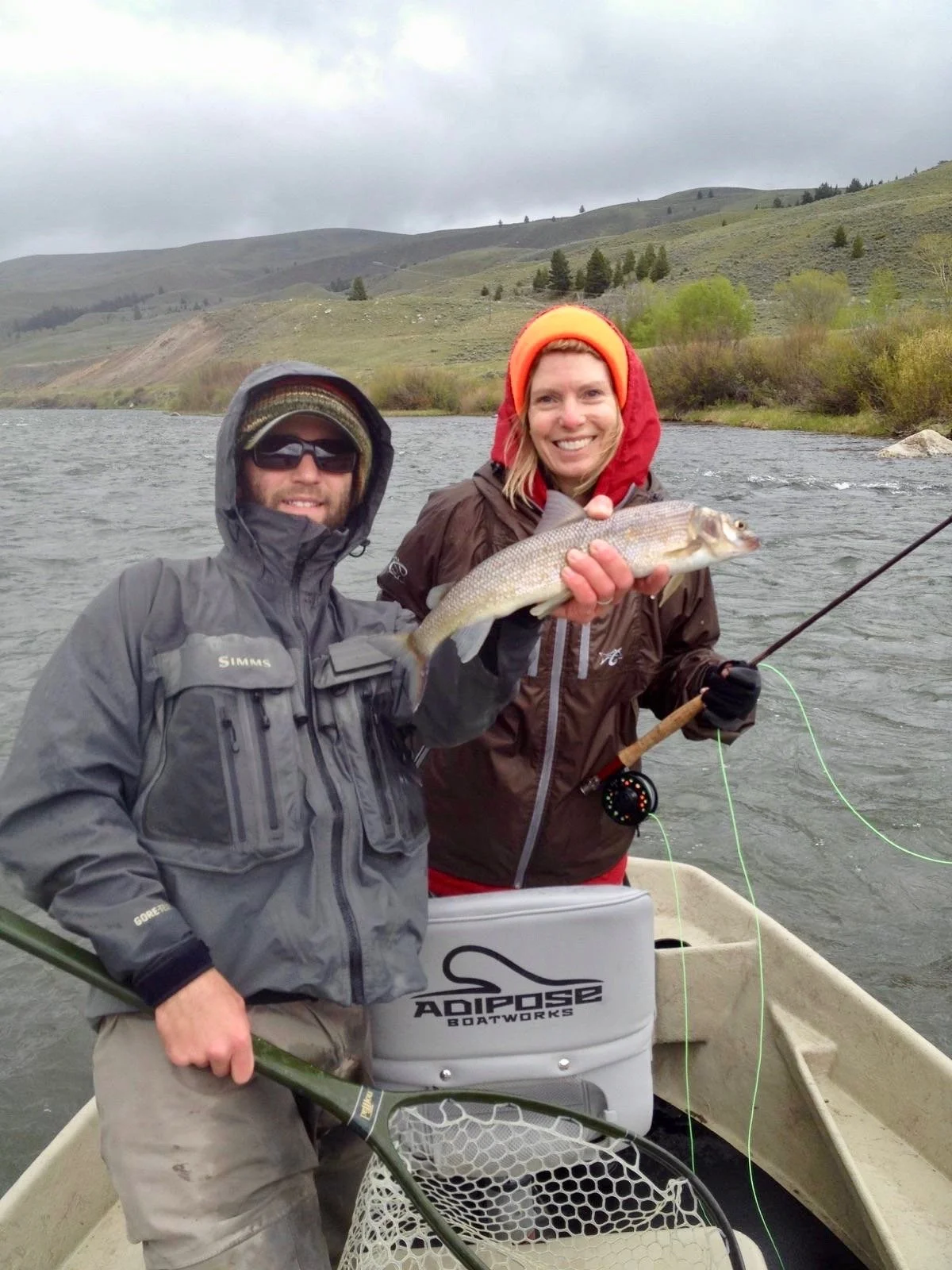 A smiling guide and bundled-up client holding a native Mountain Whitefish on a misty, cold winter day of fly fishing on the Madison River near Bozeman.
